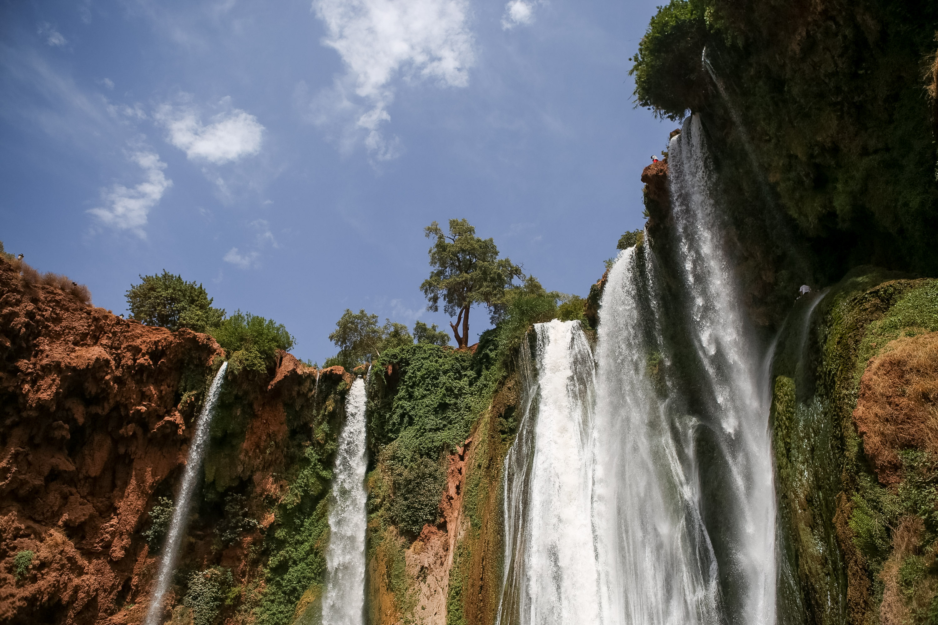 Waterfalls cascade down a cliffside surrounded by green trees under a blue sky
