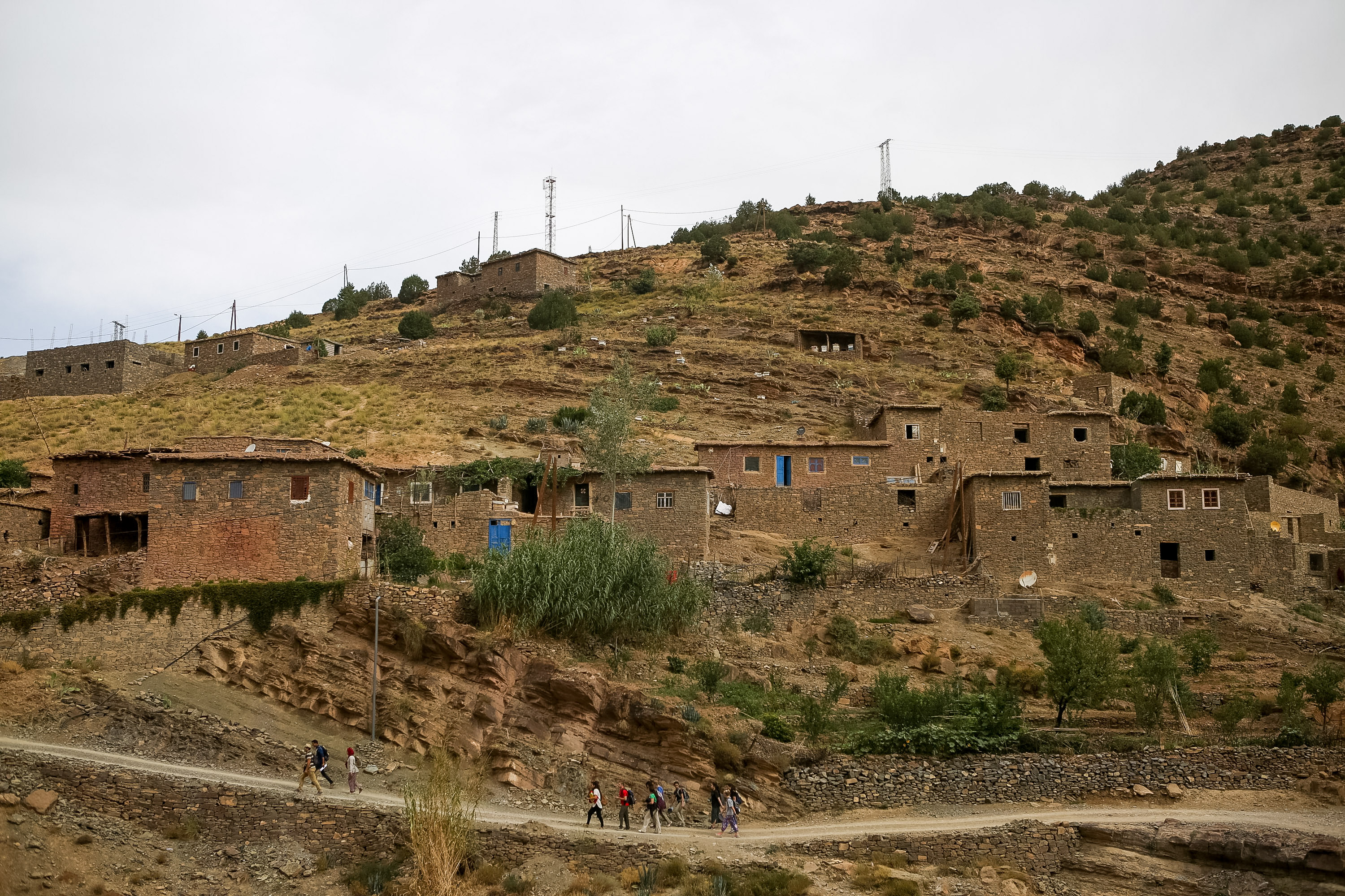 Mud-brick houses cluster on a terraced hillside above a High Atlas village path