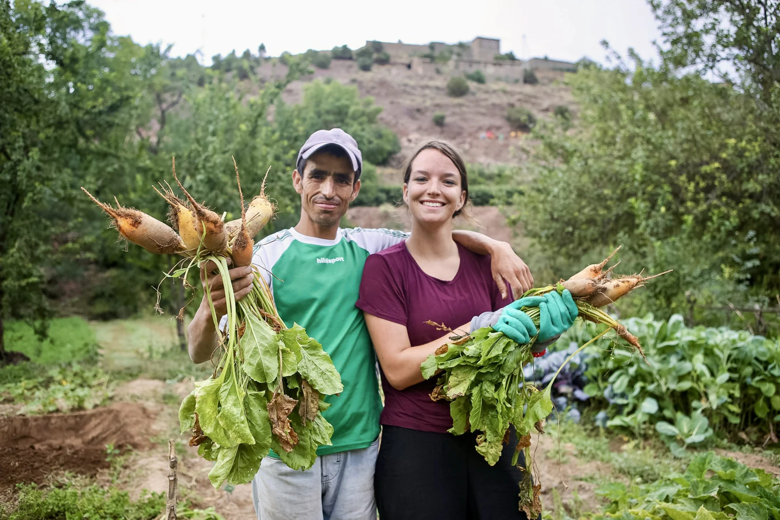 A local farmer and a student hold up bunches of freshly pulled root vegetables in a mountain garden in Morocco