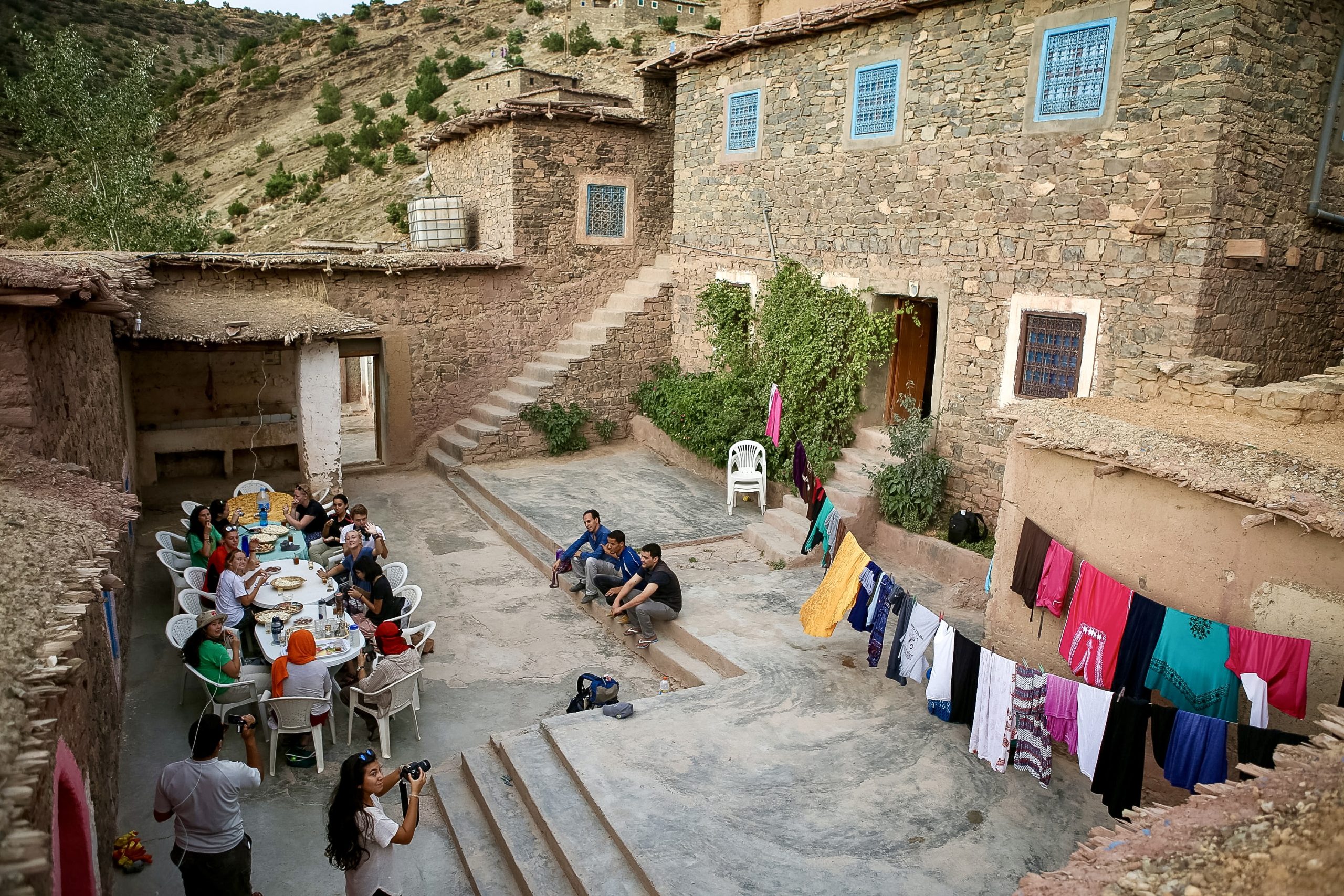 Group of students and locals sharing a meal together in the courtyard of a traditional Amazigh guesthouse in the High Atlas Mountains.