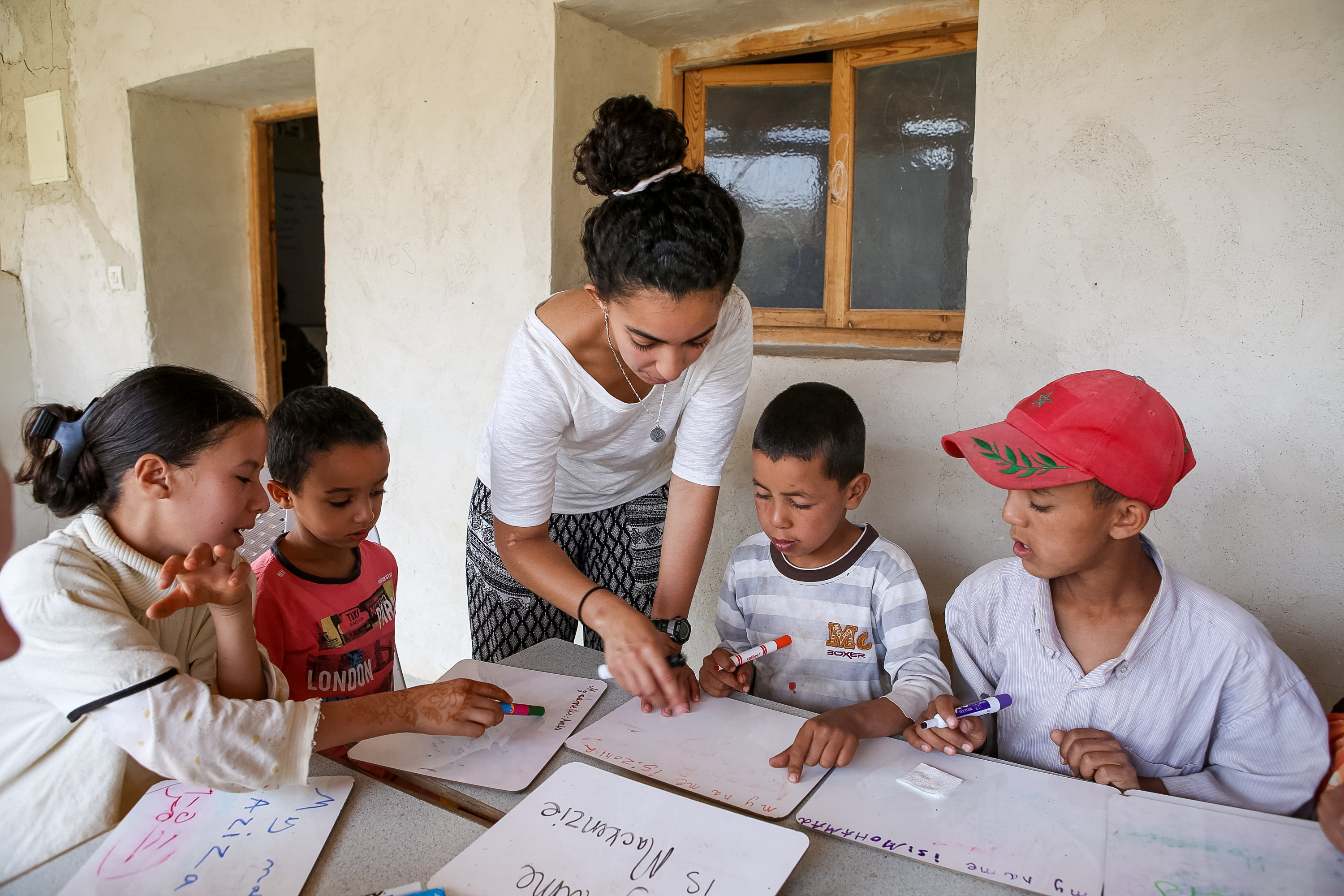 A student helps young children with a writing lesson at a table indoors in Morocco