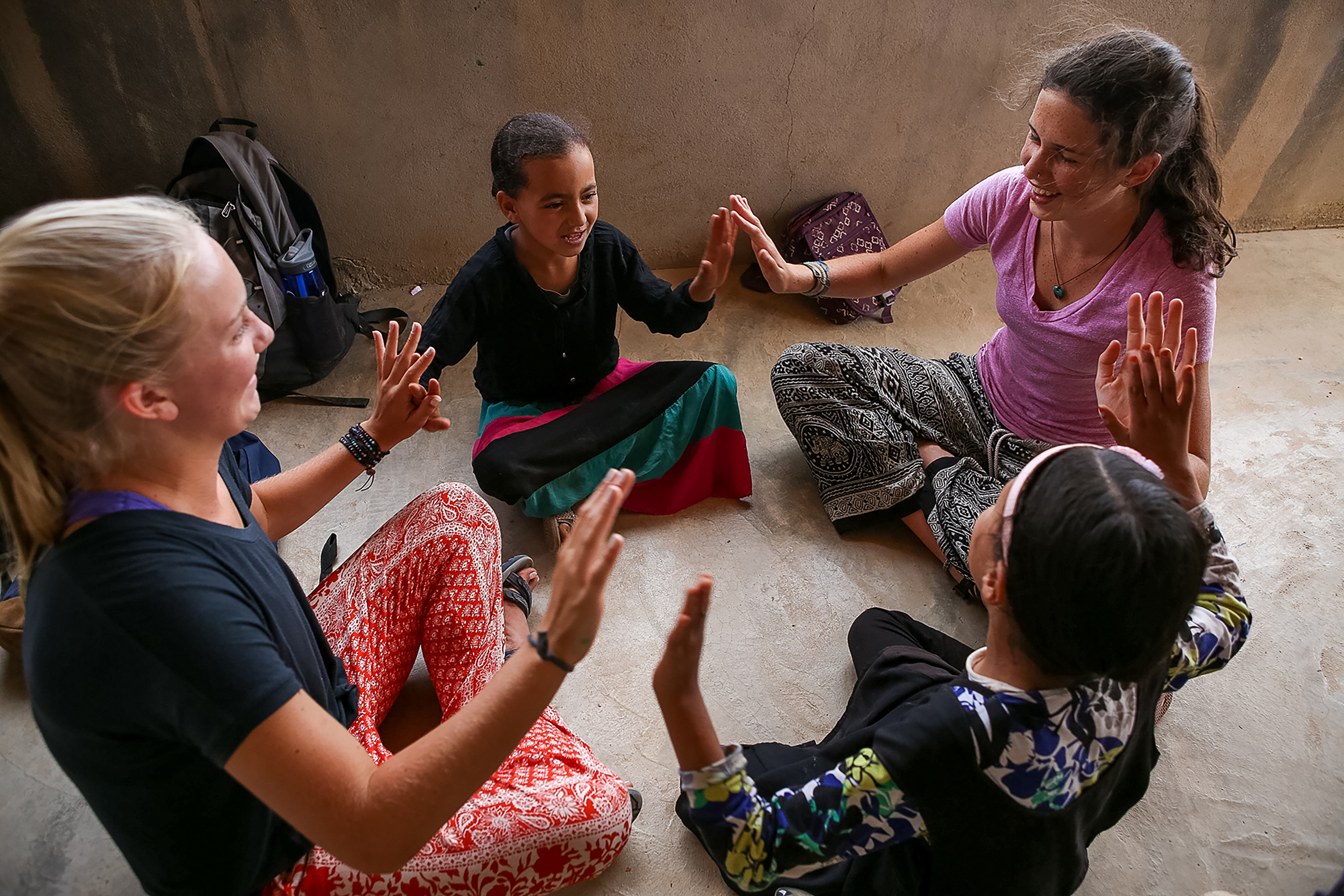Students sit in a circle playing a clapping game with a local village girl