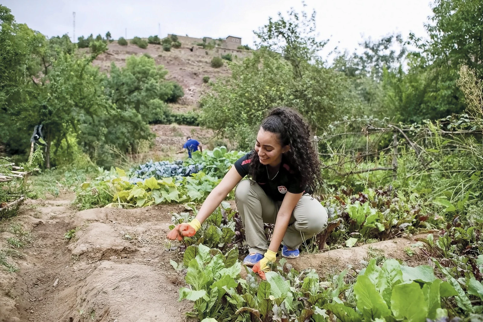 A student crouches to tend vegetables in a terraced village garden in Morocco