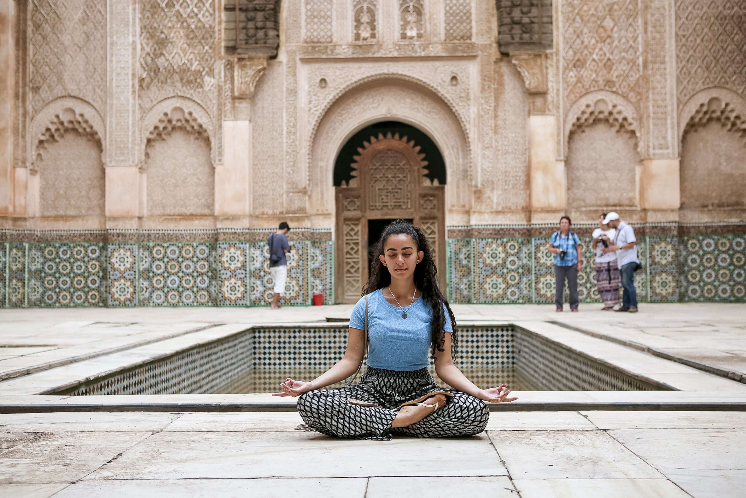 Teens sit in a meditation pose beside a courtyard pool at an ornately tiled madrasa