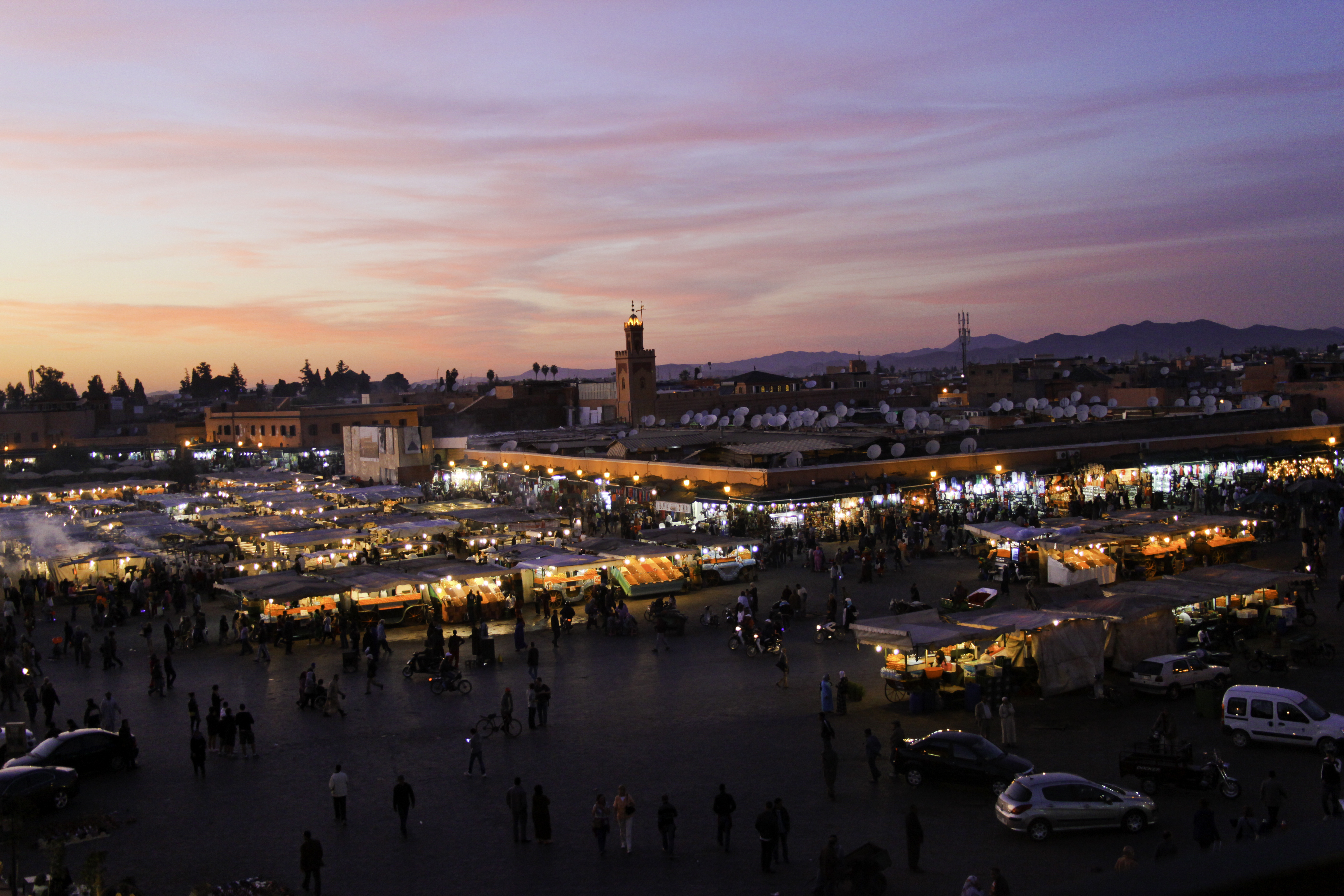 A market square in Marrakech glows with food stalls at dusk beneath a pink sky