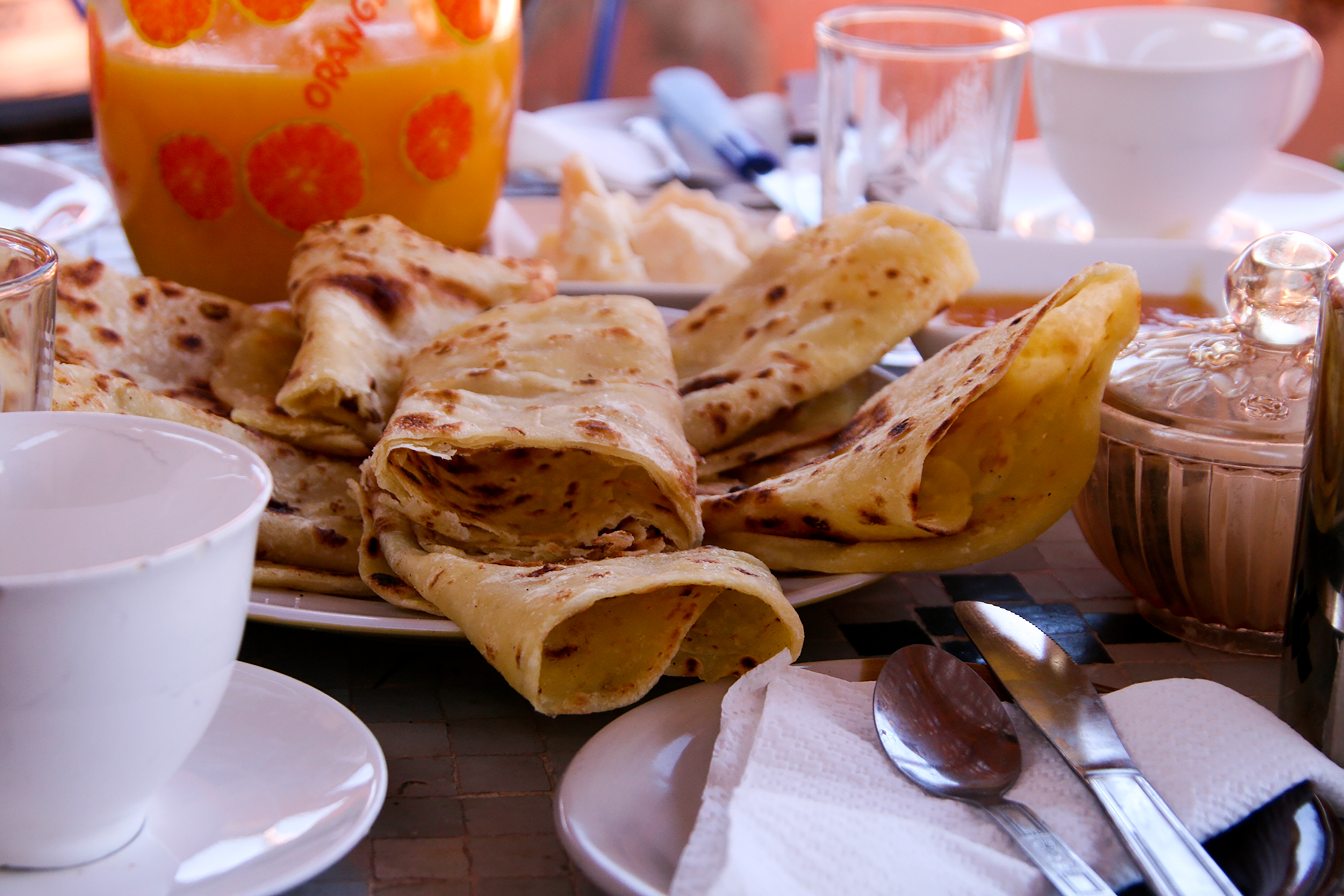 Folded Moroccan flatbreads on a plate beside fresh orange juice and coffee cups