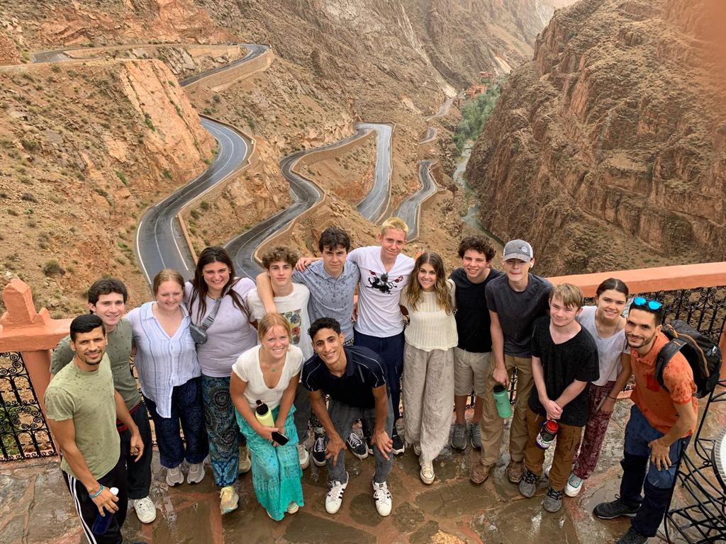 Students pose on an overlook above a winding switchback road through Moroccan mountains