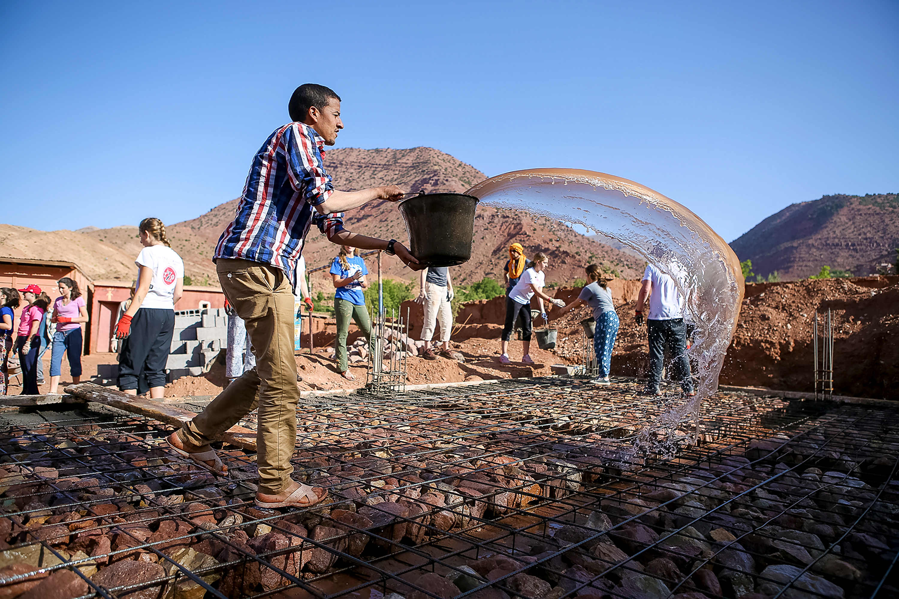 A student pours a bucket of water onto a rooftop construction site in the mountains