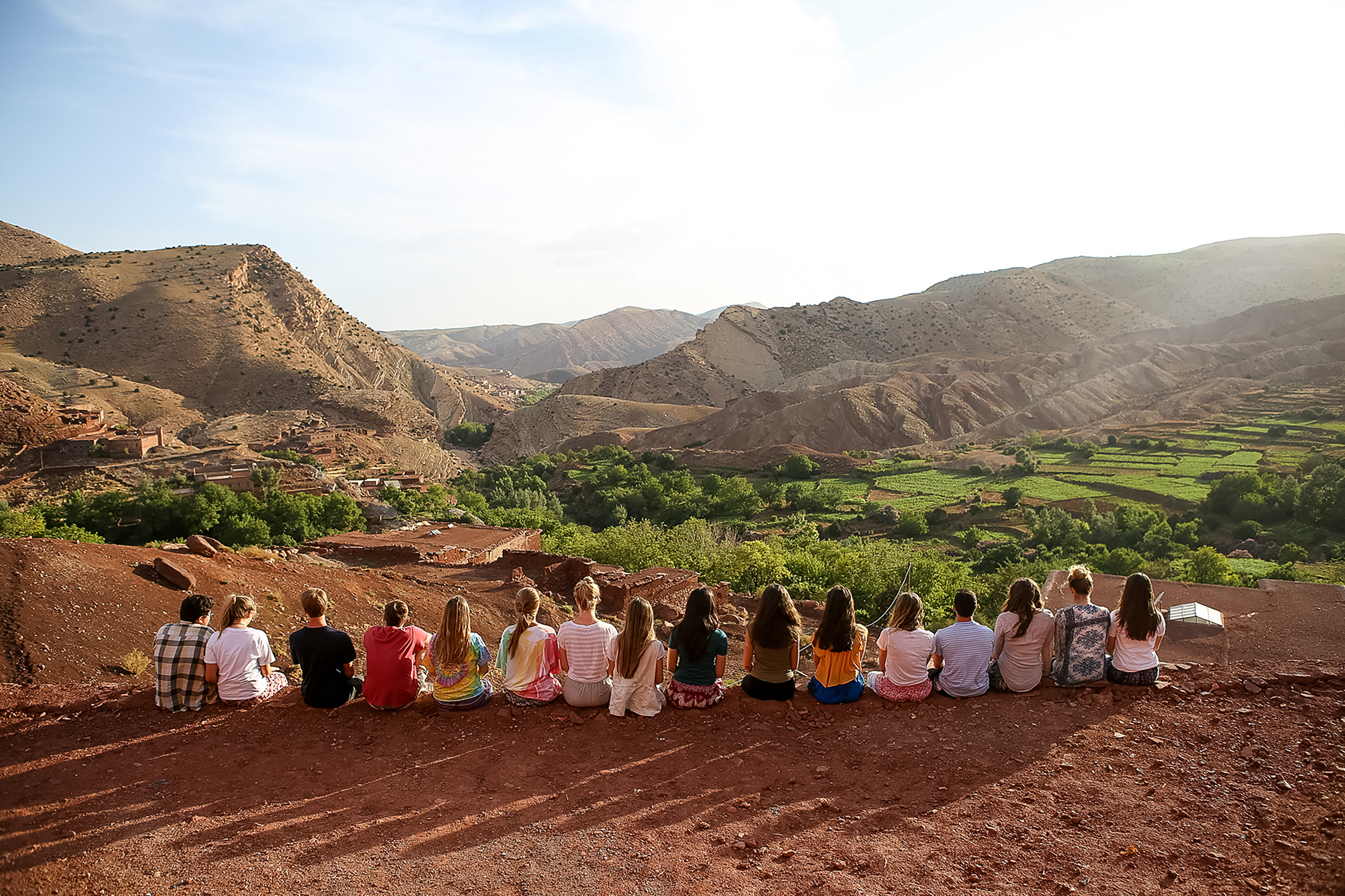 Students sit in a row overlooking terraced valleys and mountains in the Moroccan countryside
