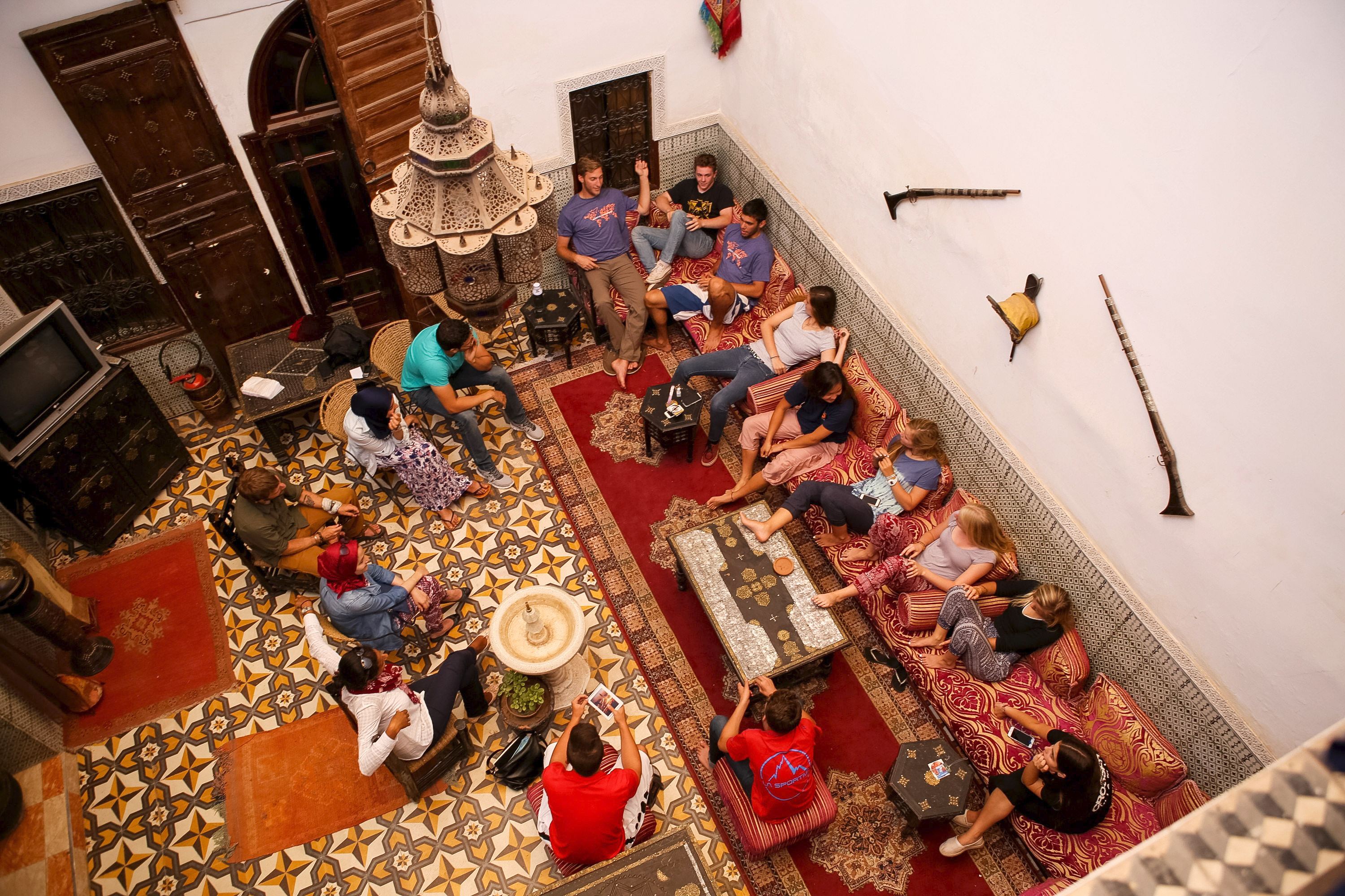 Students relax on cushioned seating in a tiled traditional Moroccan riad, viewed from above