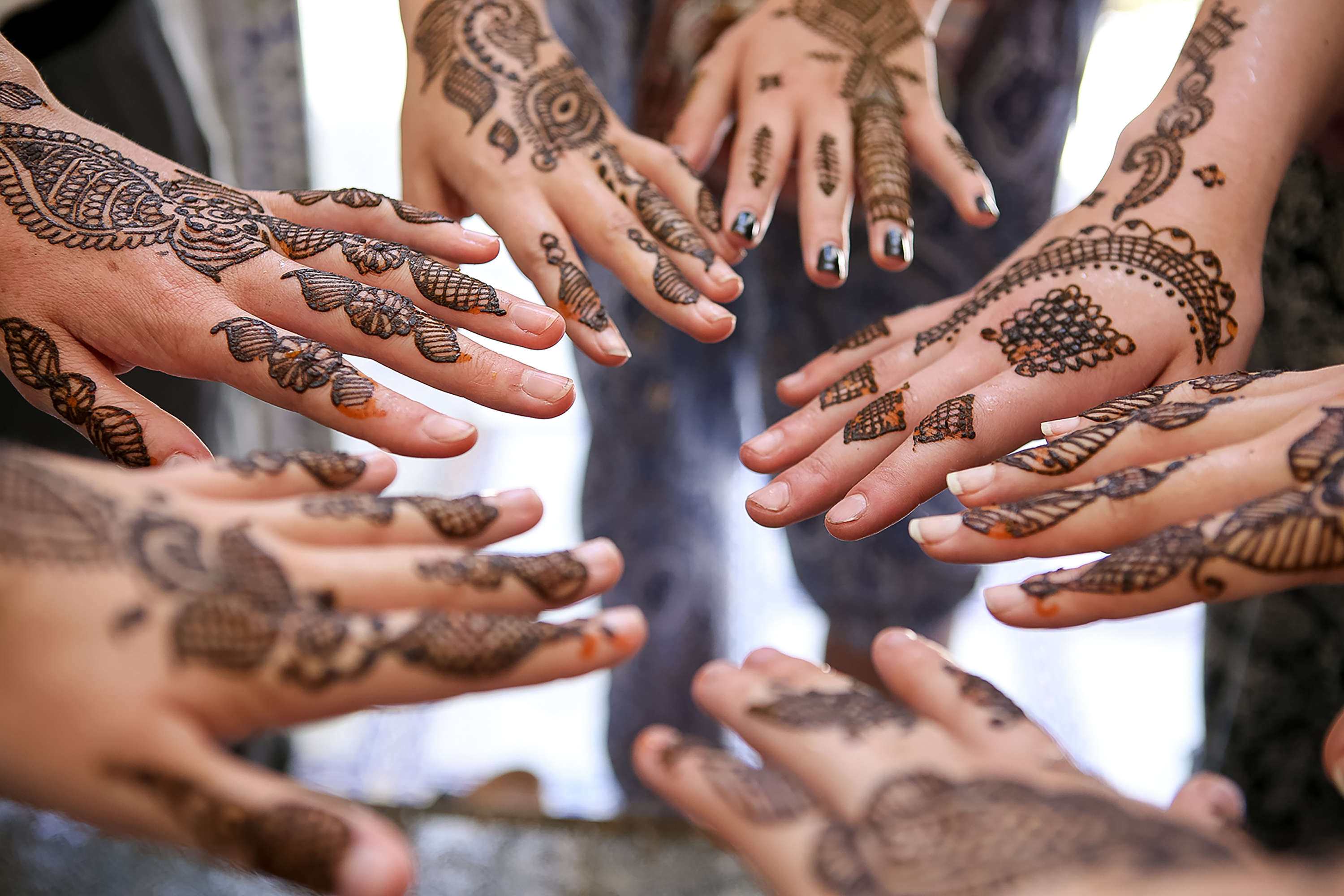 Hands decorated with intricate henna designs reach toward each other in a circle