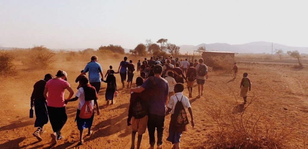 A group of students and local children walking along a dusty path in an open, rural area. Life Skills For Teens