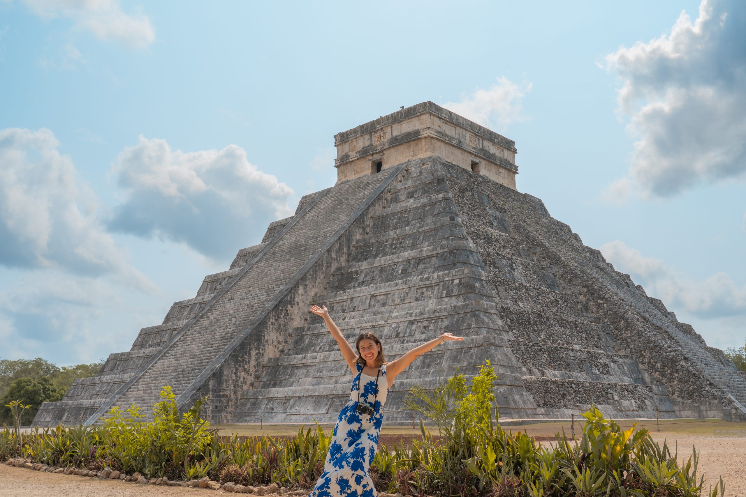 A student raises her arms in celebration in front of the Chichen Itza pyramid