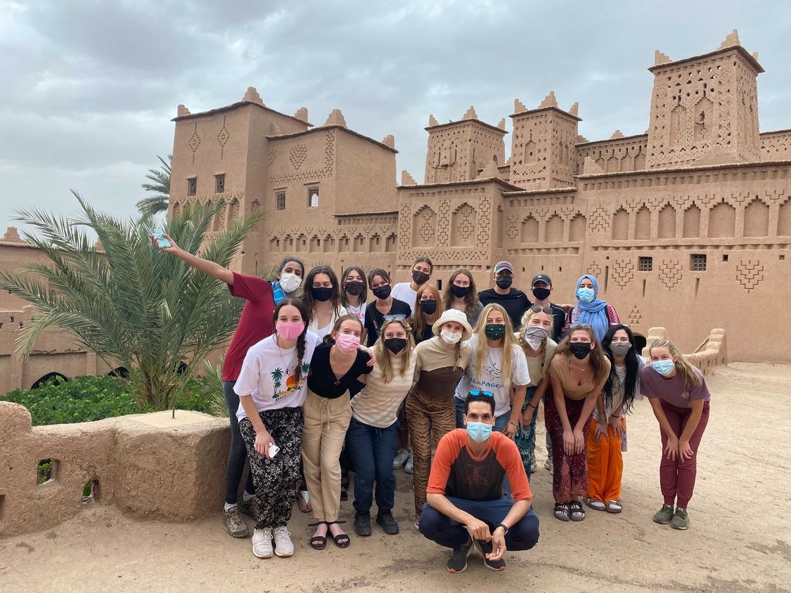 Students in masks pose together outside a mudbrick kasbah in Morocco