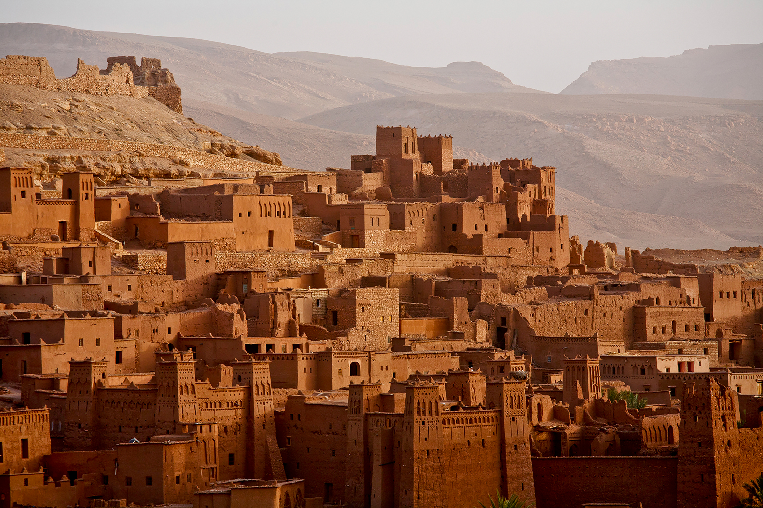 Mudbrick kasbah buildings cluster on a hillside beneath rugged mountains in Morocco