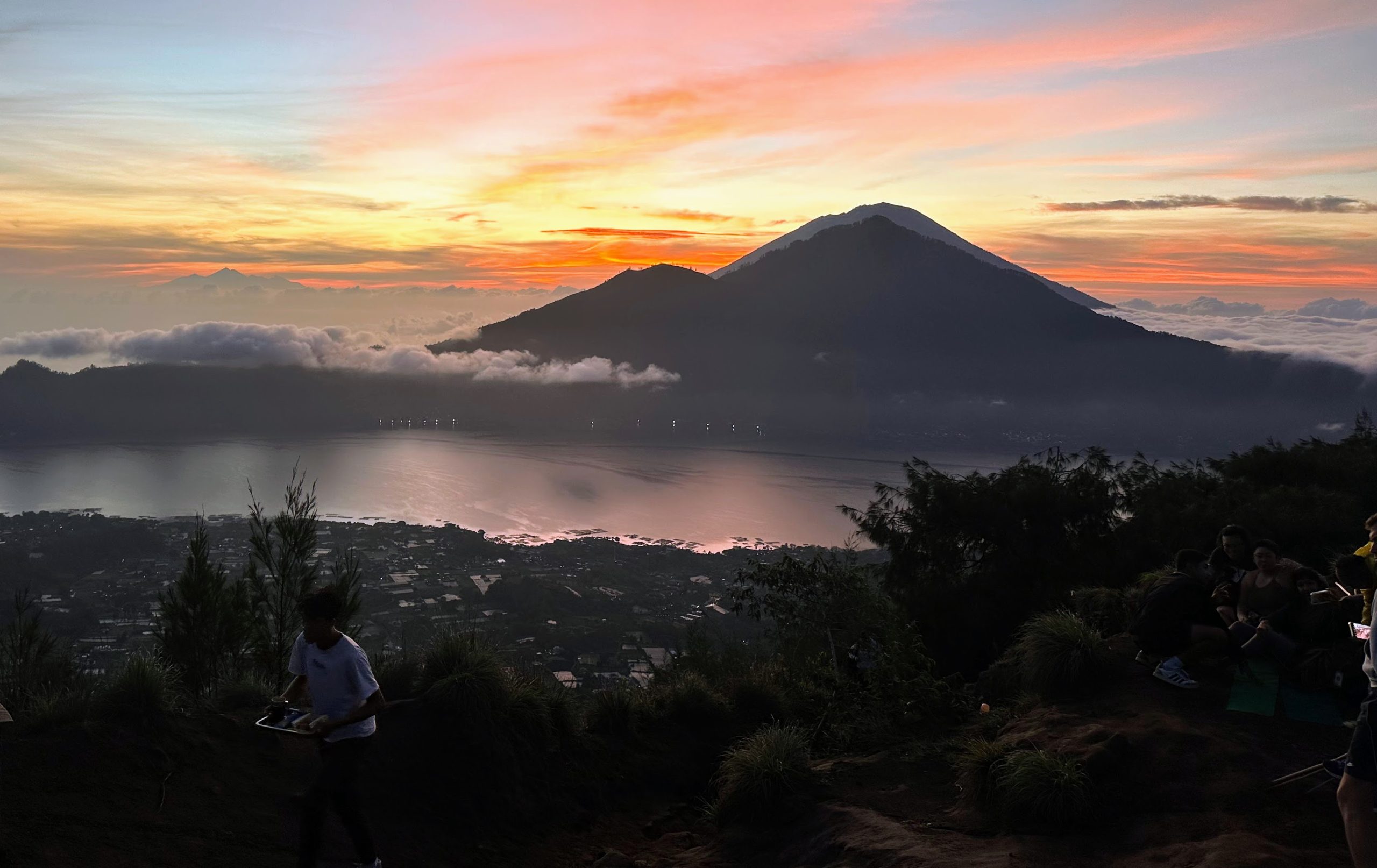 A stunning sunrise view over Mount Batur with clouds rolling over the lake and the mountain in the distance.