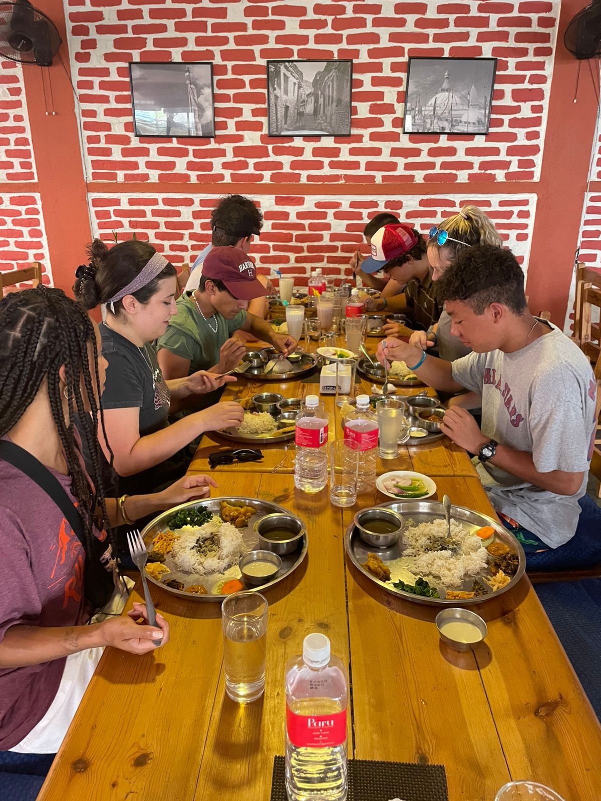 Students eat a rice and lentil meal from steel plates at a long wooden table.