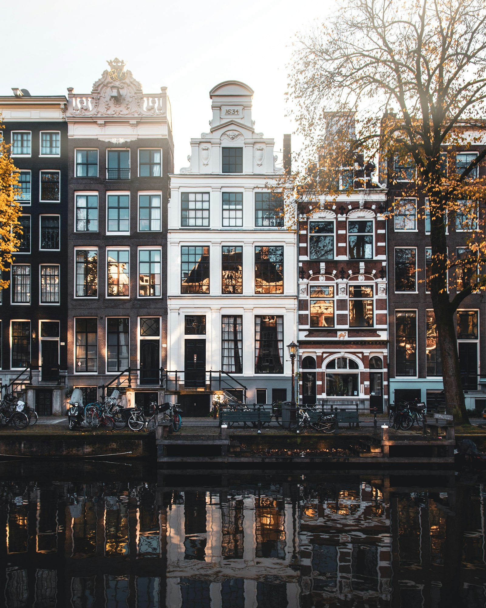 Four Amsterdam canal houses at dusk, one white front carrying the date 1634, with bicycles racked along the quay below.