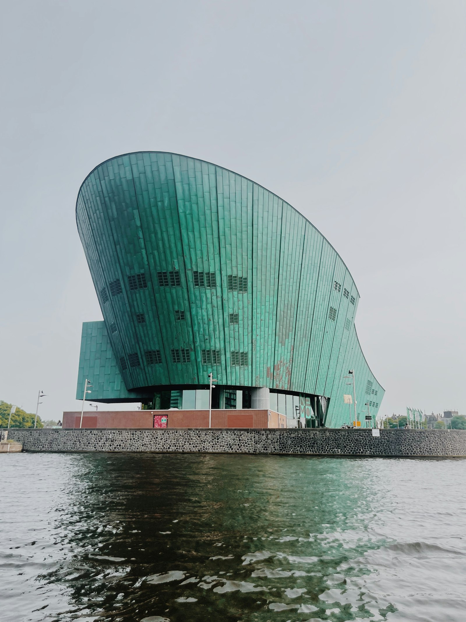 The green copper hull of the NEMO Science Museum rising out of the water in Amsterdam under a flat grey sky.