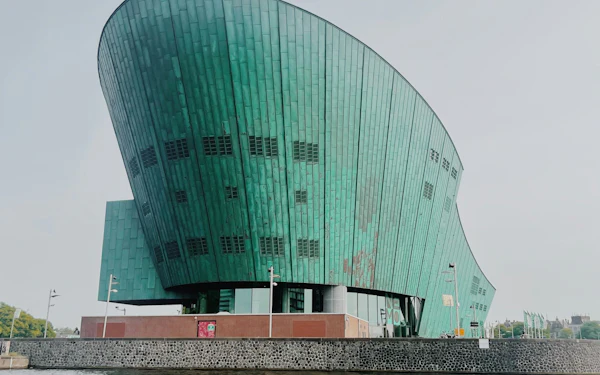 The green copper hull of the NEMO Science Museum rising out of the water in Amsterdam under a flat grey sky.