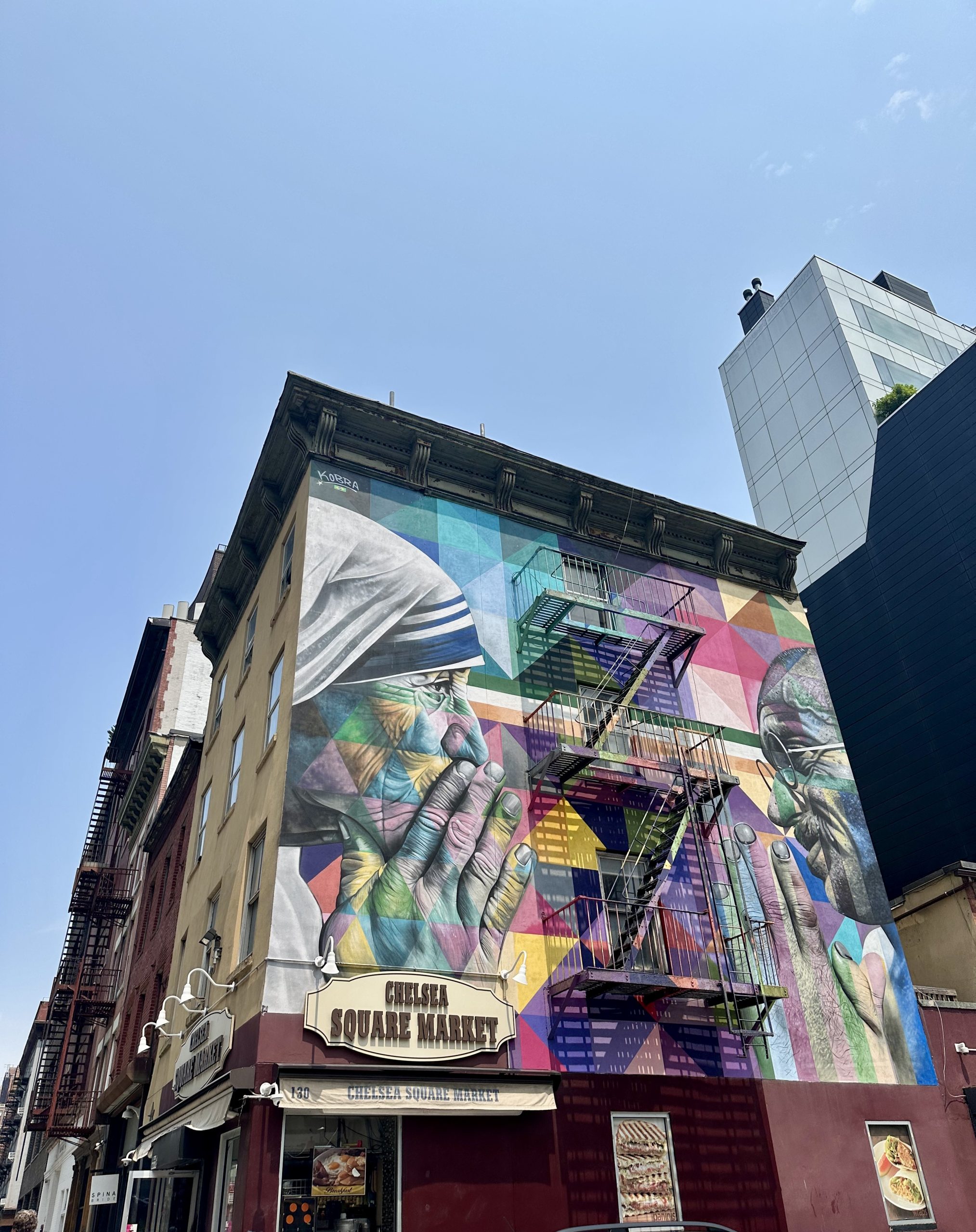 A colorful mural of hands and faces, common in street art in the United States, covers the side of the Chelsea Square Market building