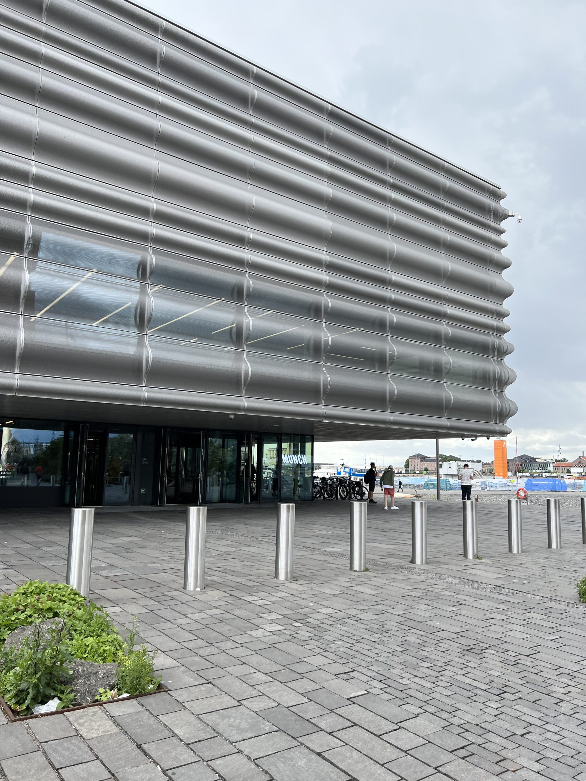 A modern building with a rippled metal facade sits beside a waterfront plaza