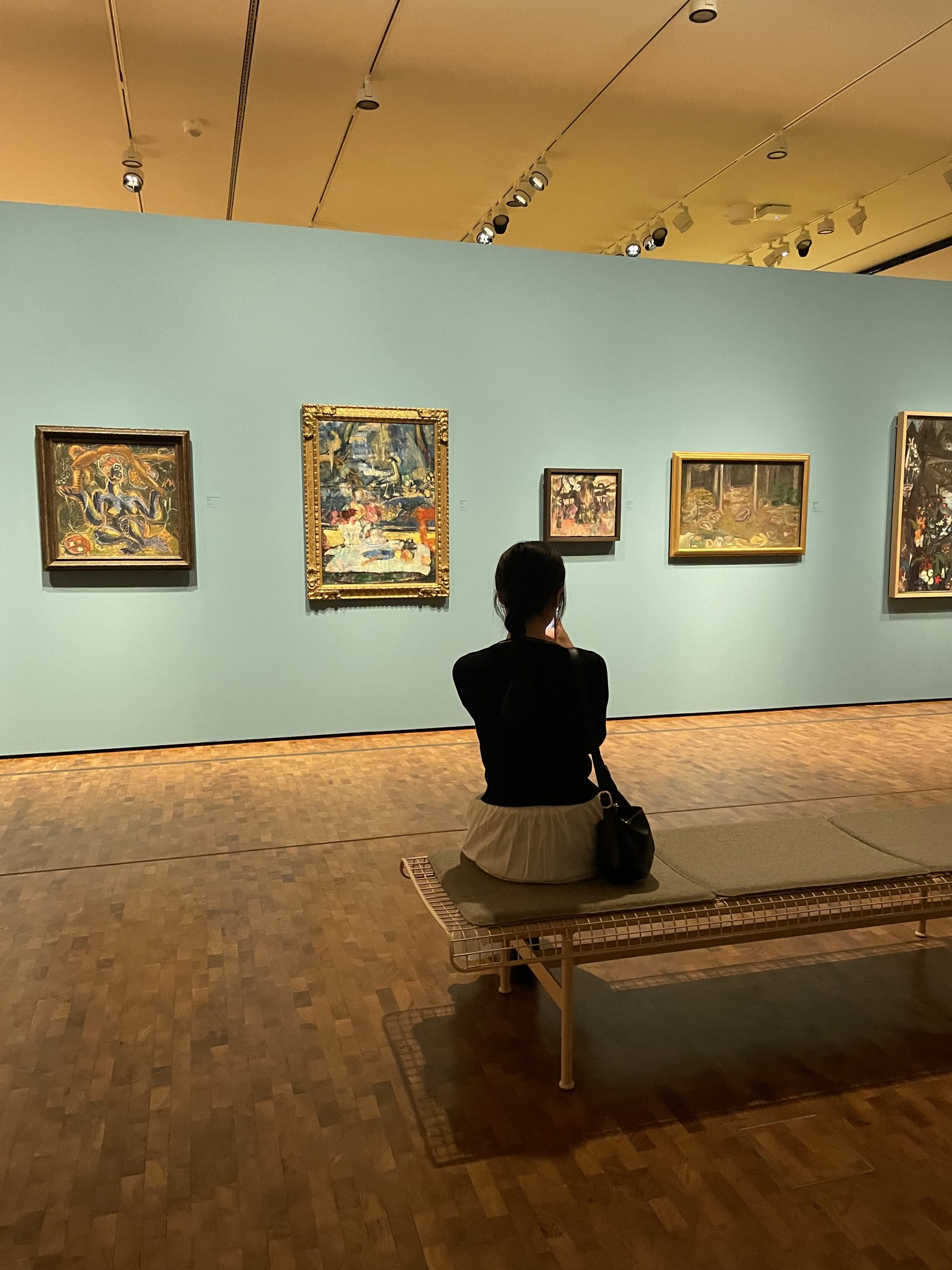 Teens sit on a gallery bench viewing framed paintings on a museum wall