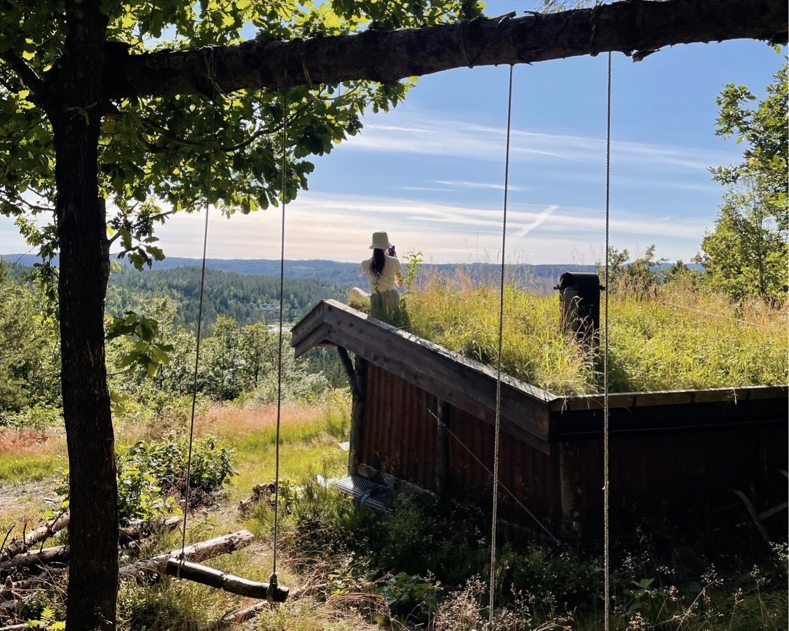 A student stands atop a grass-roofed cabin overlooking rolling hills