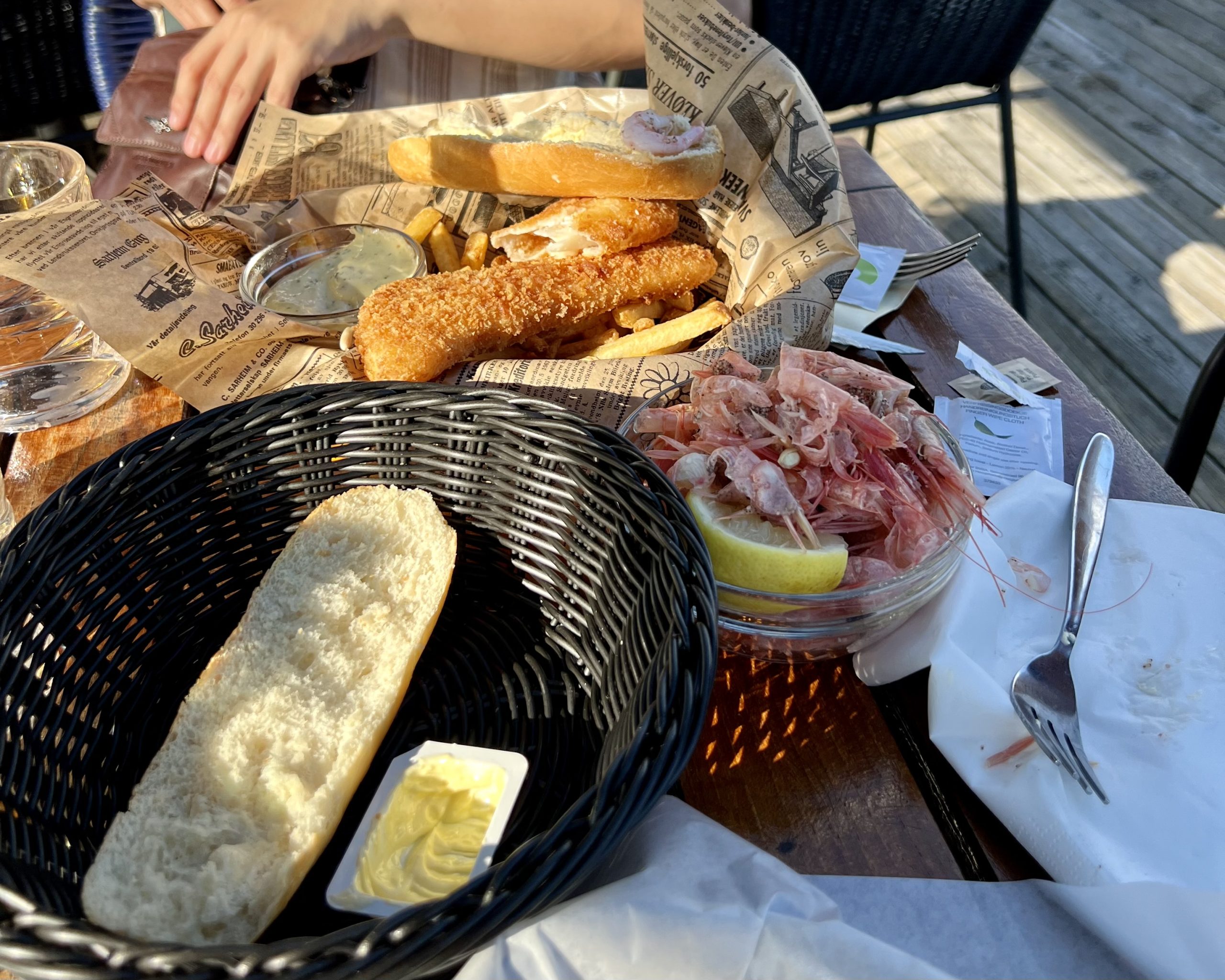 An outdoor table set with fried fish, bread, shrimp, and lemon at an open-air restaurant