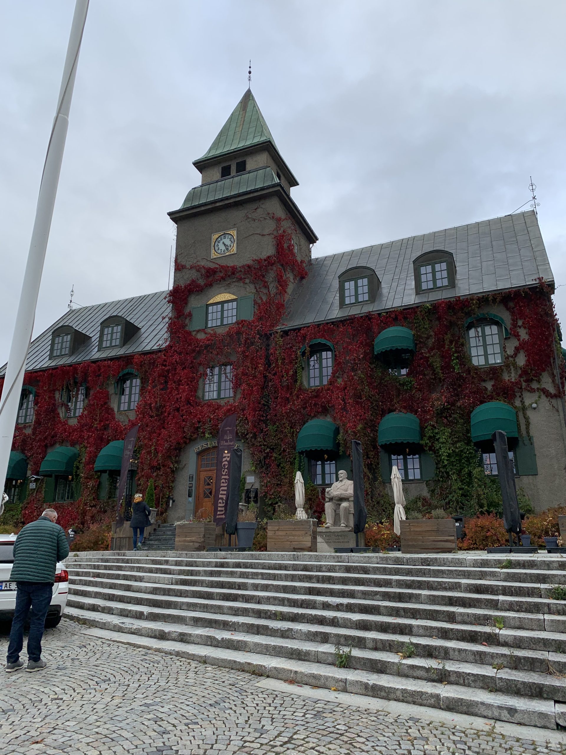 A clock tower building covered in red autumn ivy, seen from a stone staircase