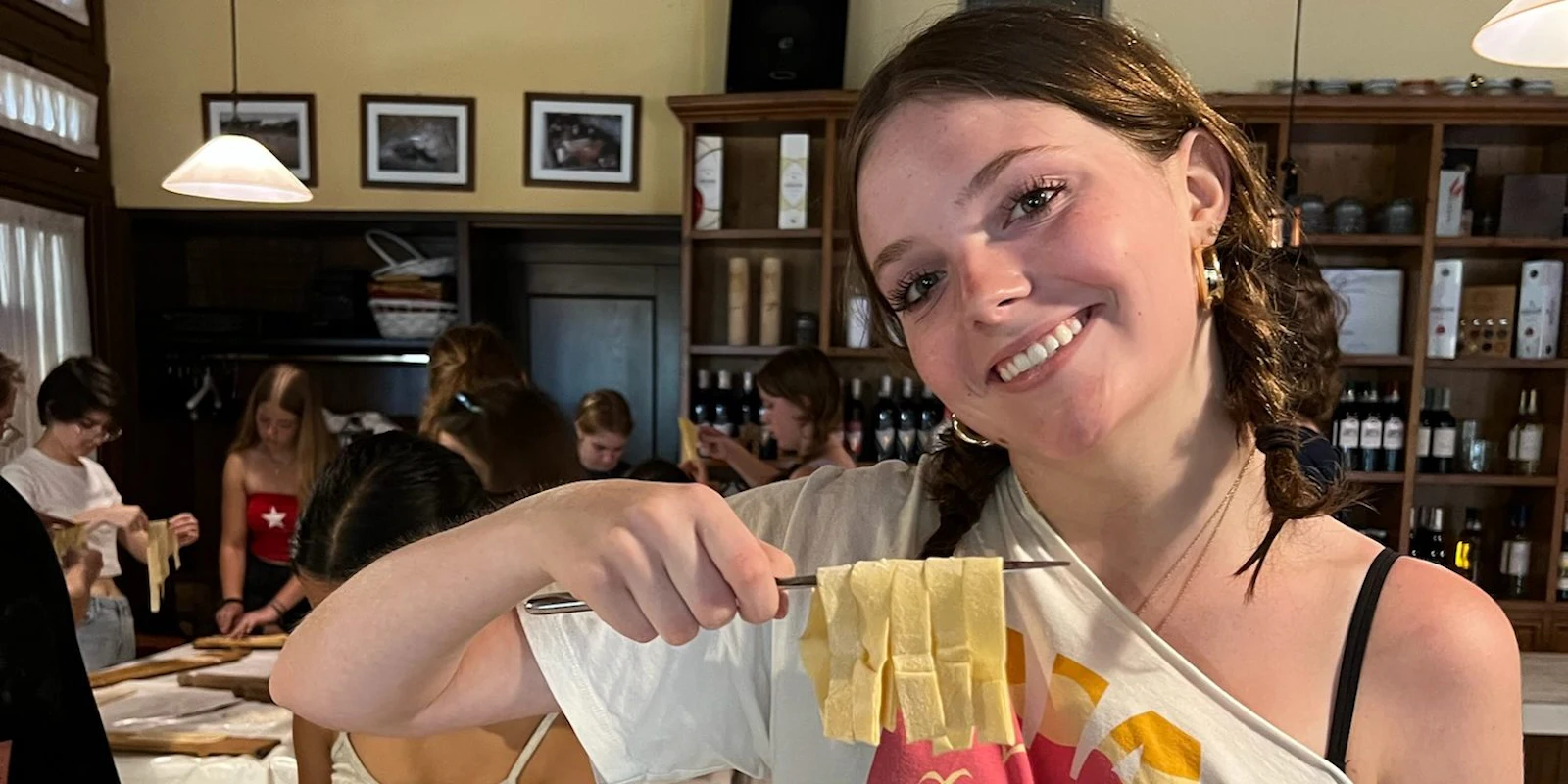 A teen traveler smiles as she holds up ribbons of fresh pasta at a cooking class in Italy