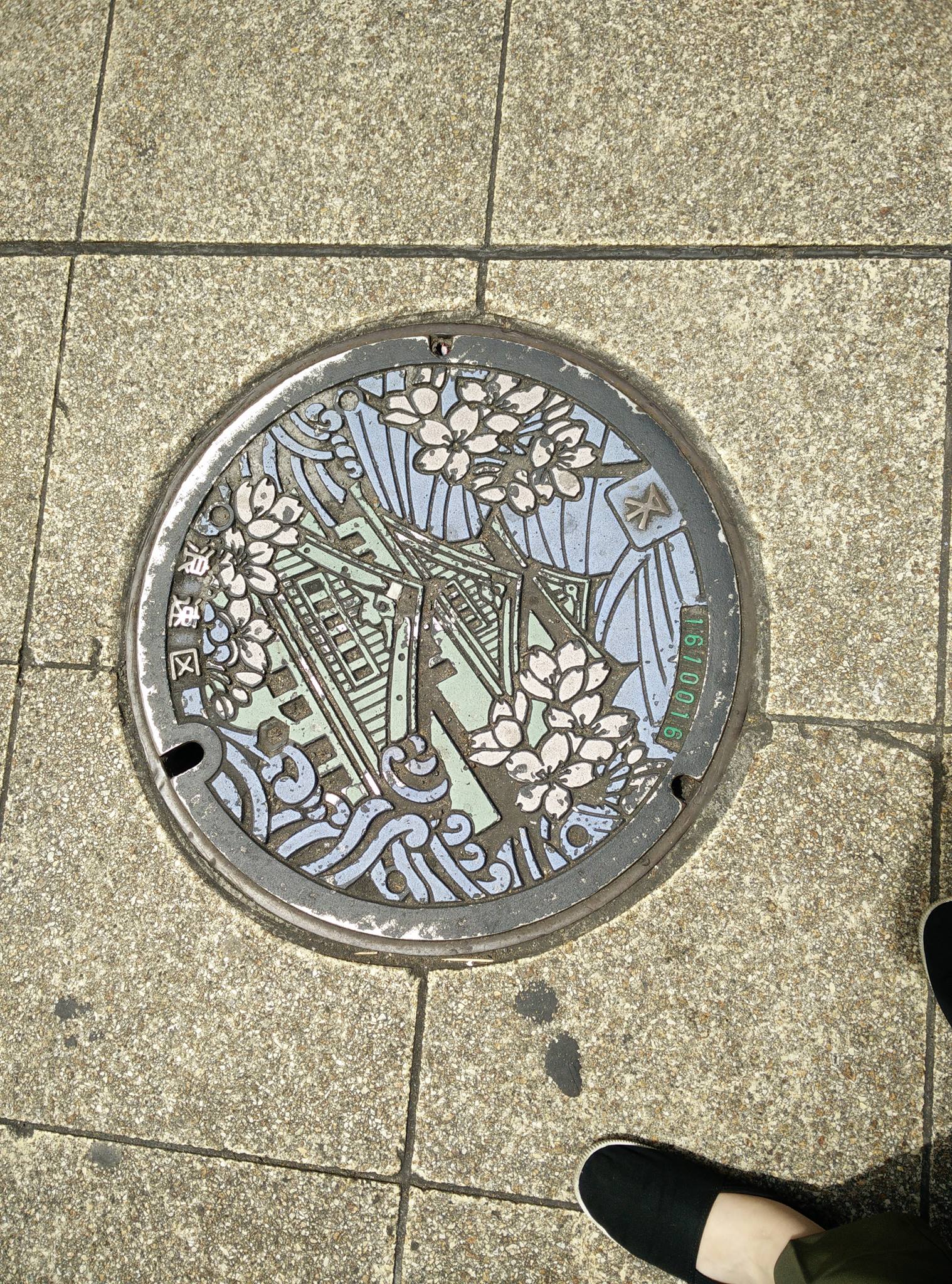 A colorful manhole cover depicting Osaka Castle surrounded by cherry blossom petals.