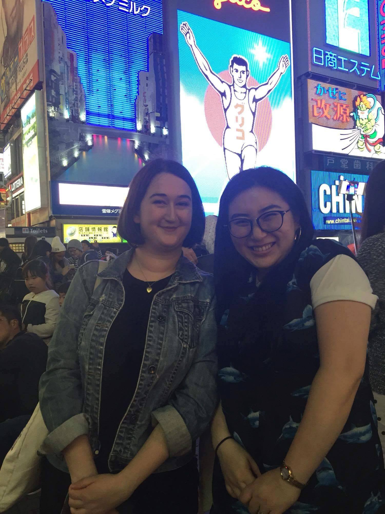 Emma and Sayuri stand in front of the Glico running man sign at night in Dotonbori.