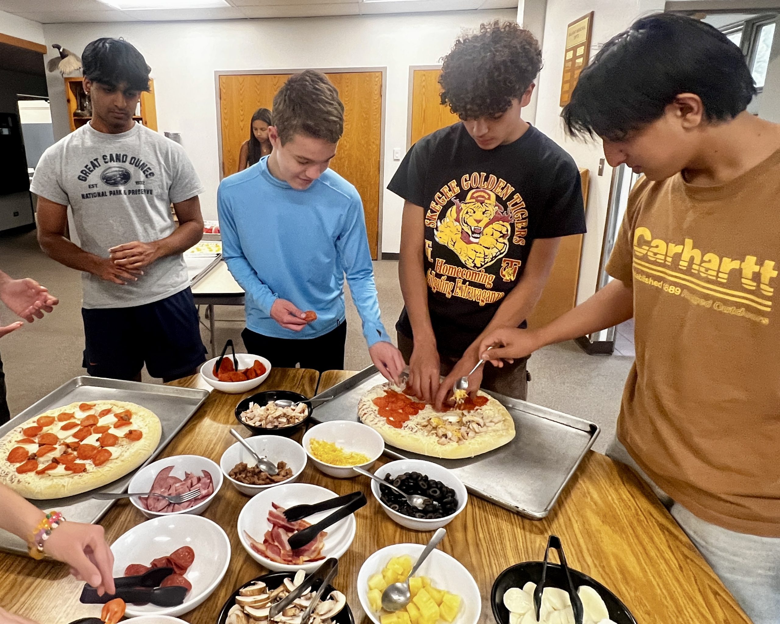 Teens add toppings to homemade pizzas during dinner prep at a Colorado outdoor adventure camp.