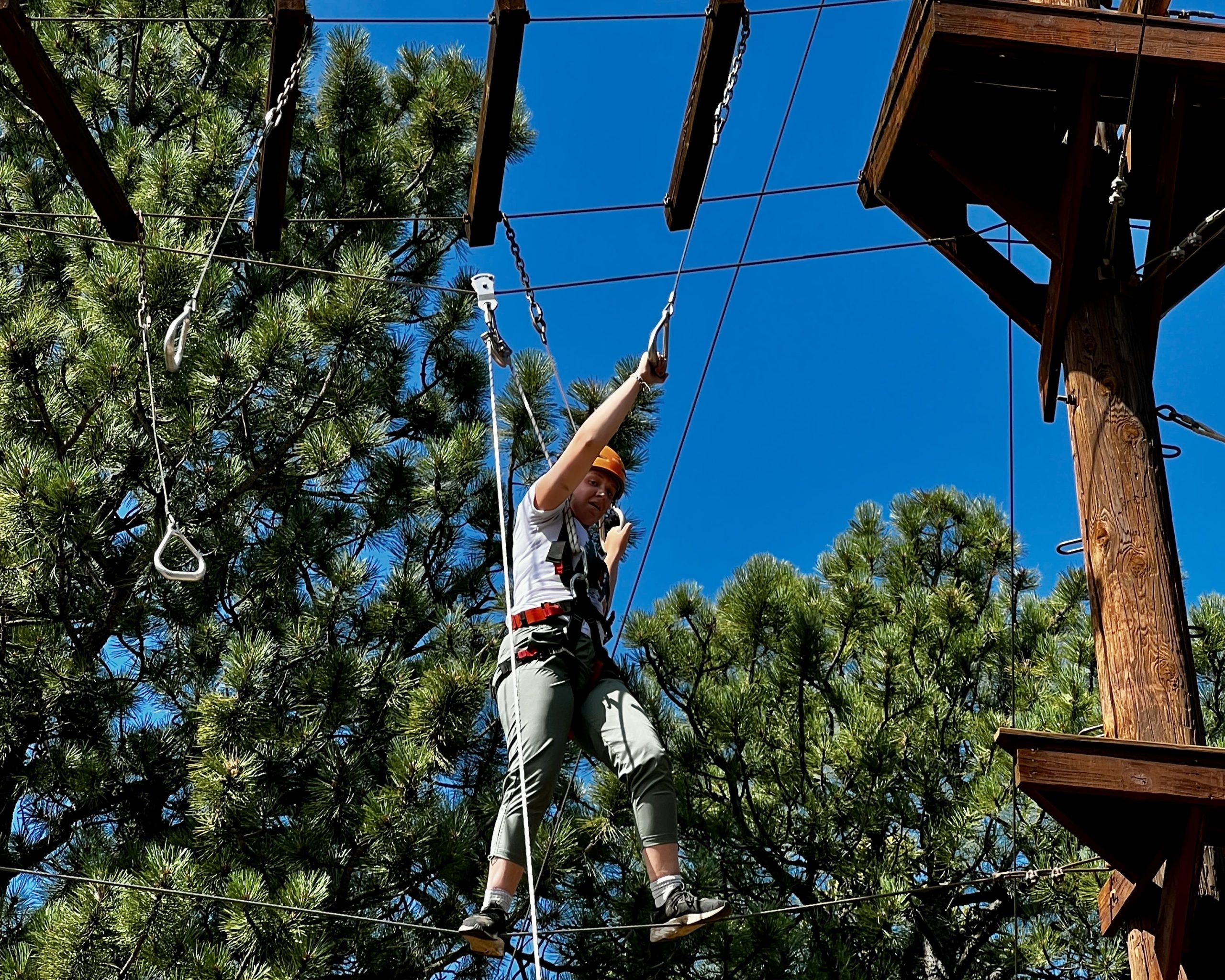 Camper crosses a suspended high ropes element above the trees at a Colorado adventure camp near Denver.
