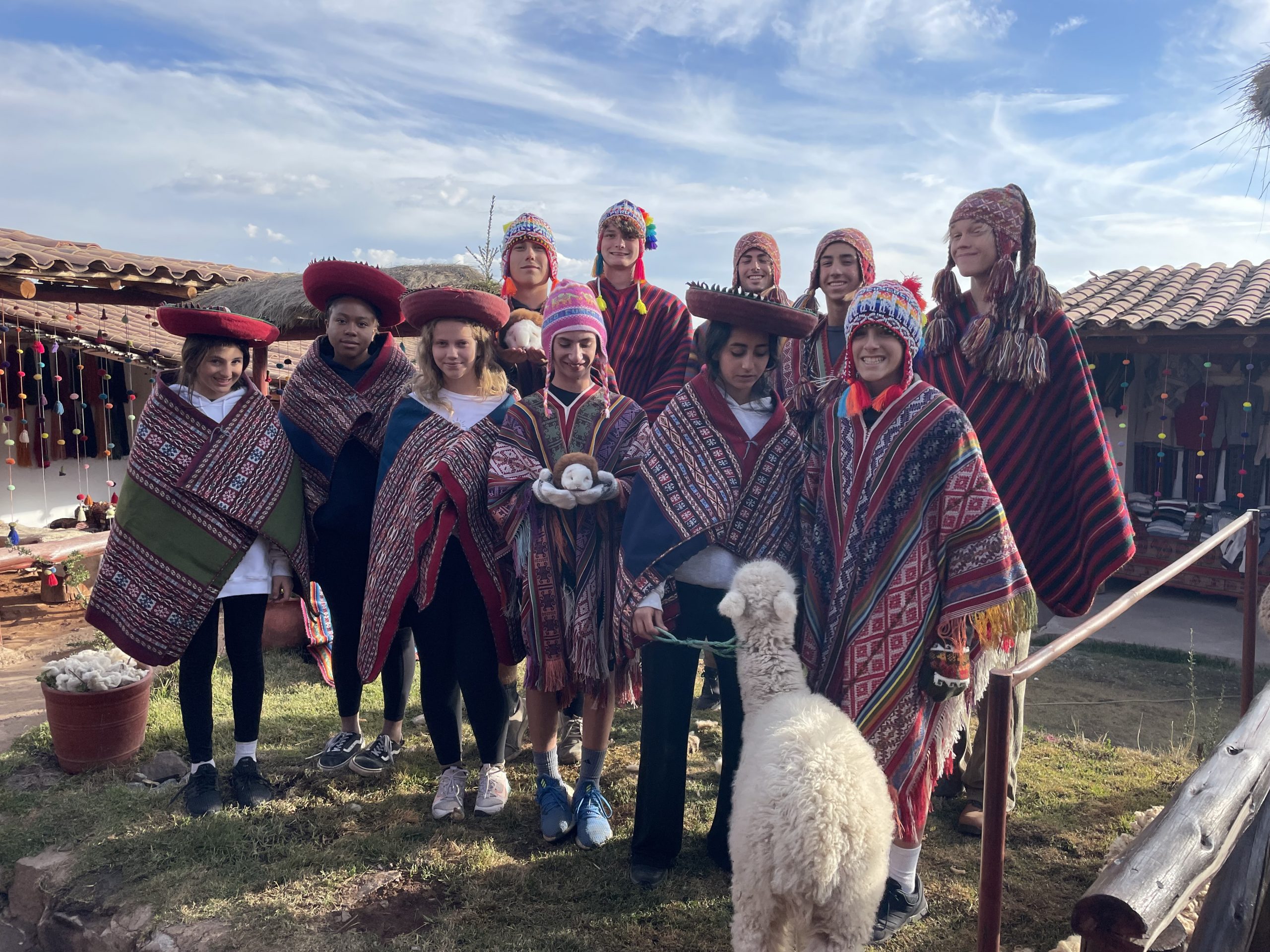 Students in traditional Andean ponchos and hats pose with an alpaca