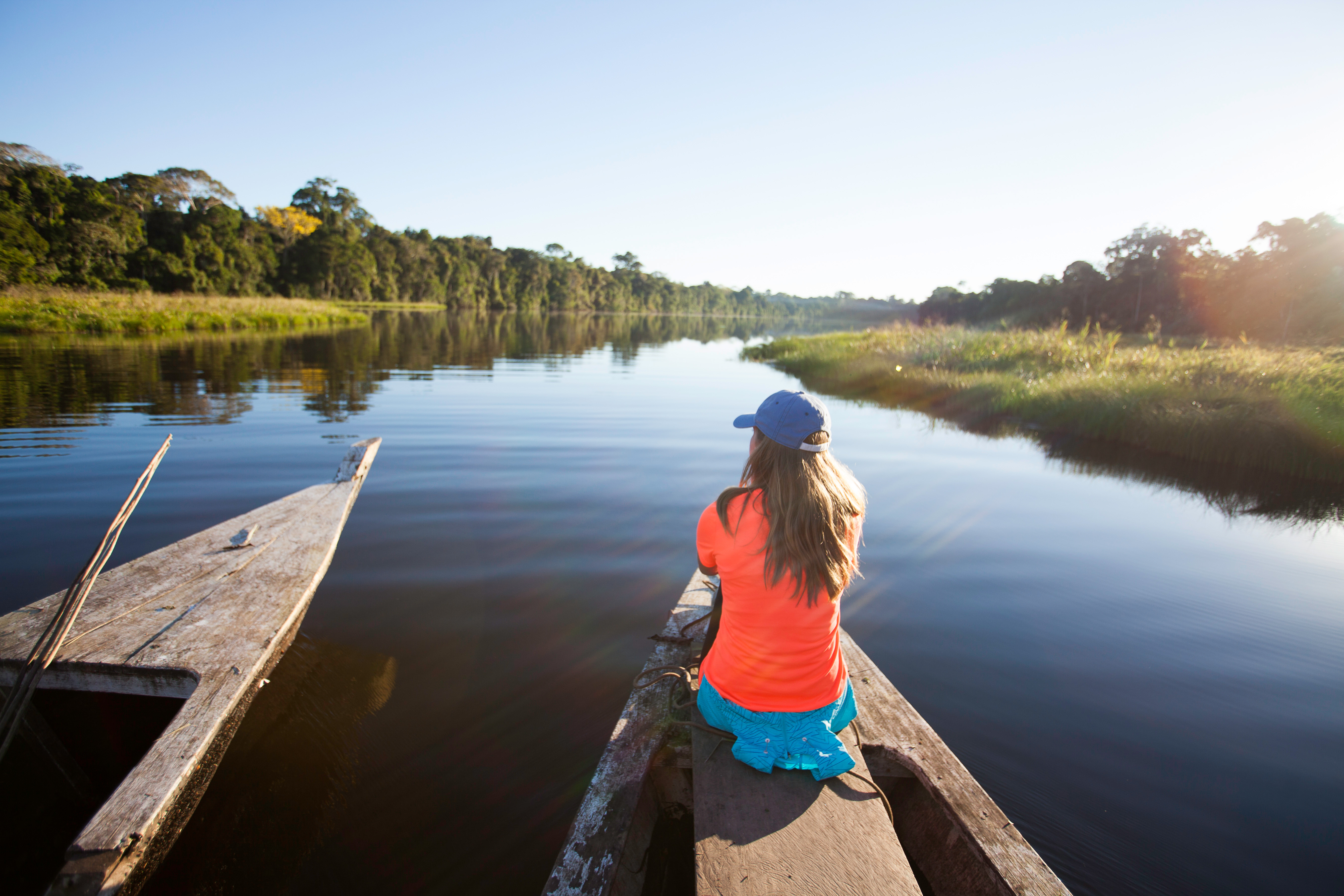 Woman sitting in a canoe on a calm river surrounded by forest.