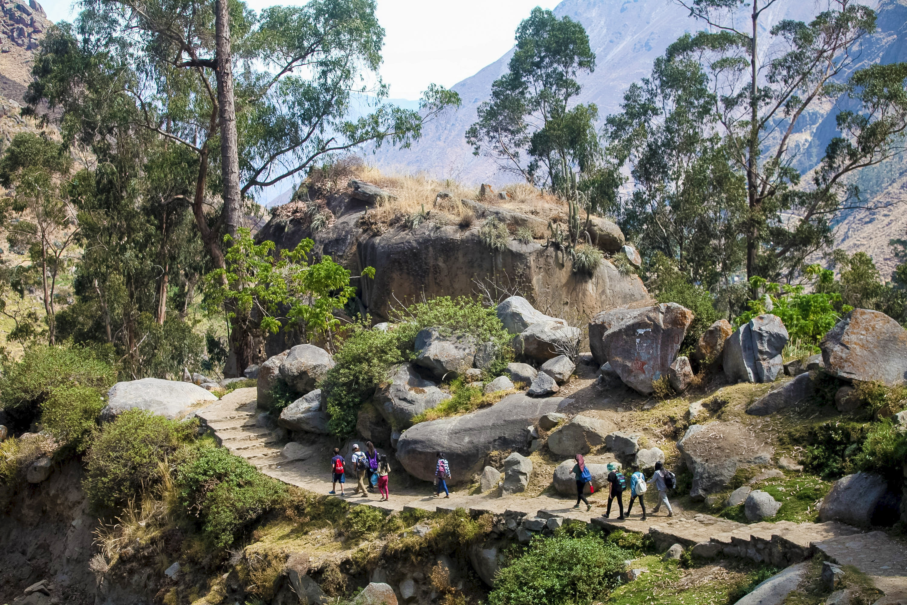 A school trip pauses on a stone path near boulders along a mountain trail in Peru