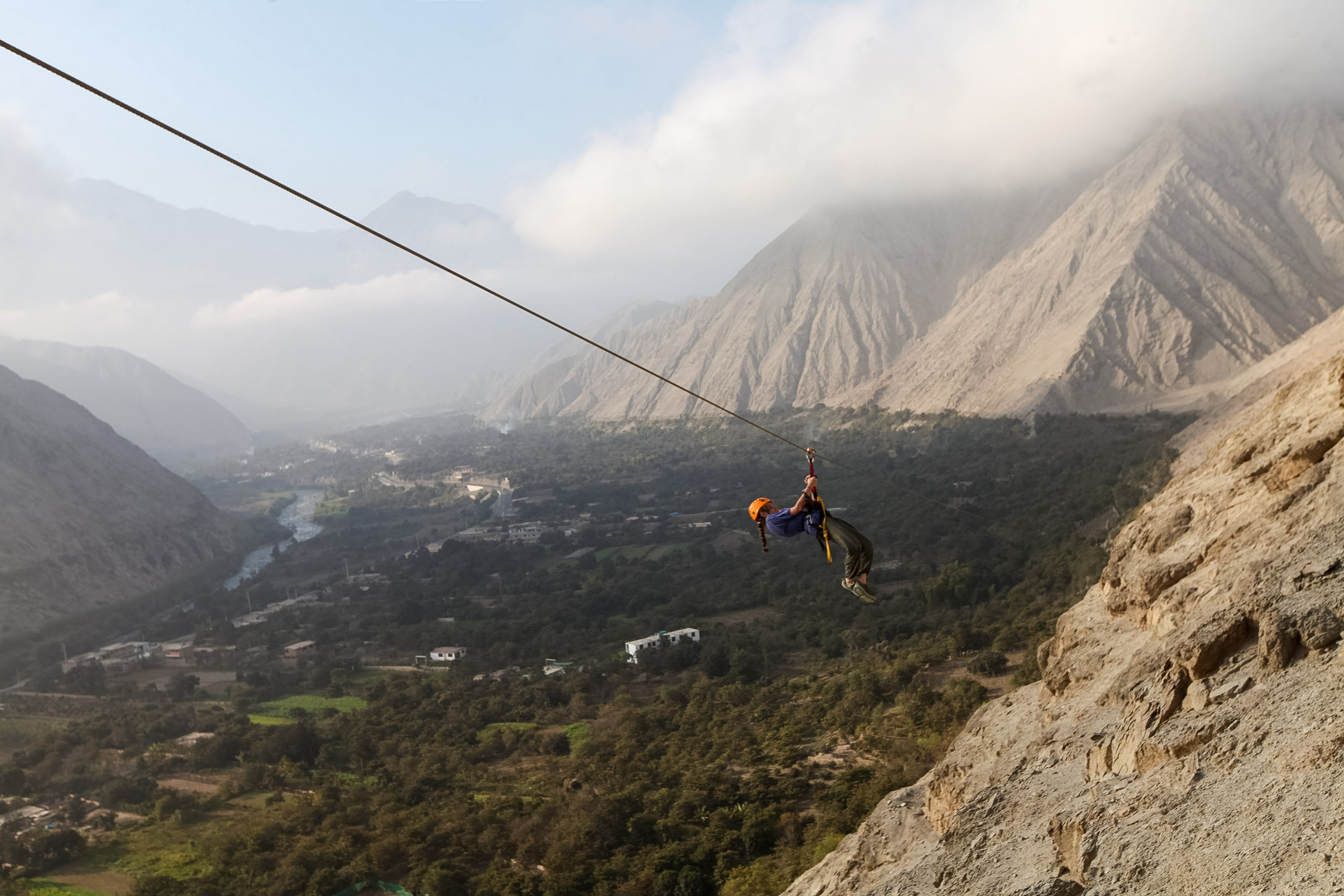 A student ziplines above a green valley with mountains in the background