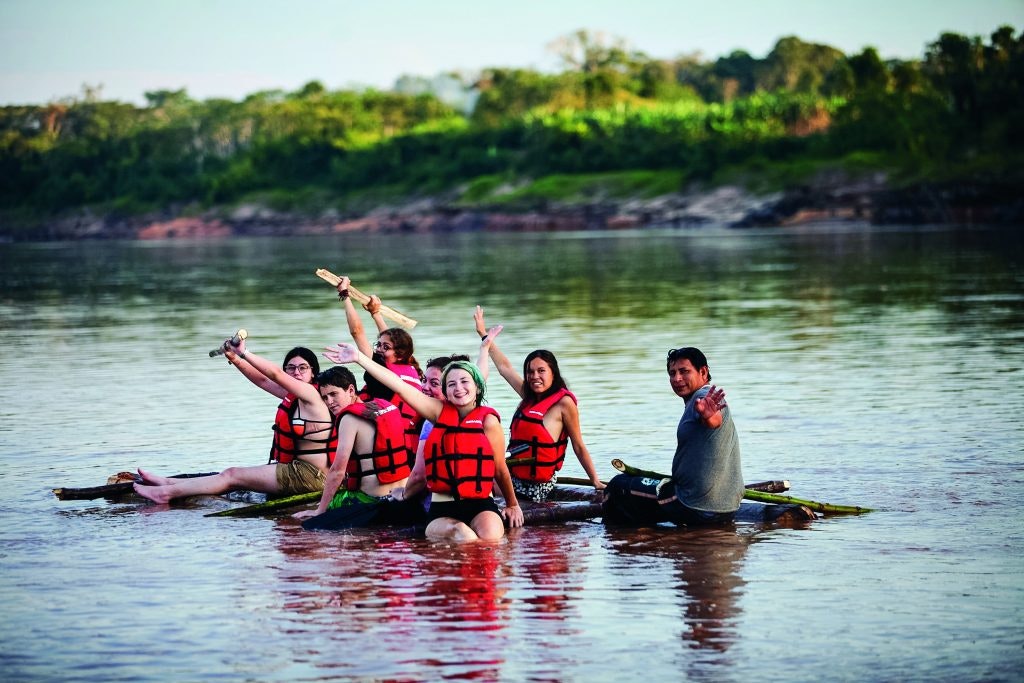 Student travelers on waving from a raft on the Amazon River during a Peru teen tour.