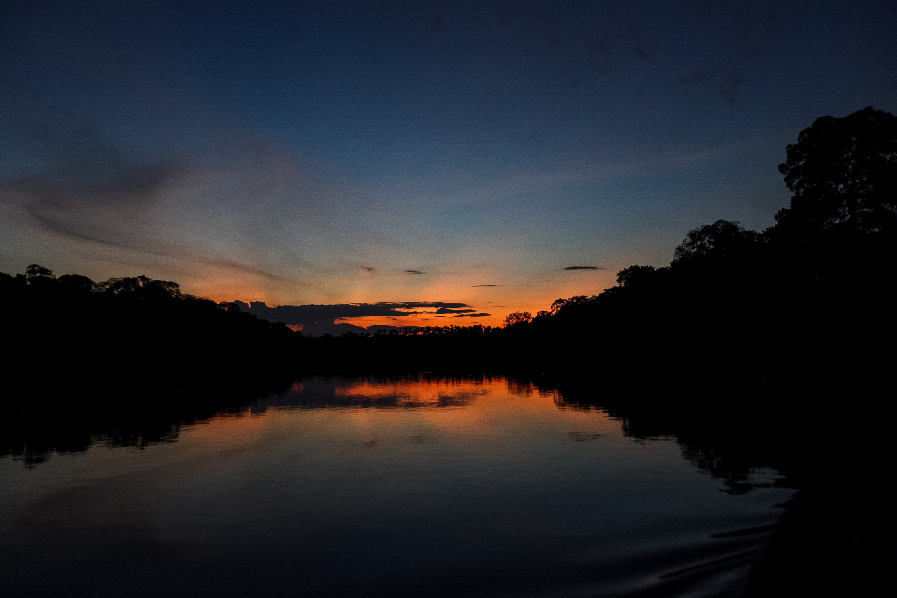 Sunset silhouettes the treeline over a calm Amazon river