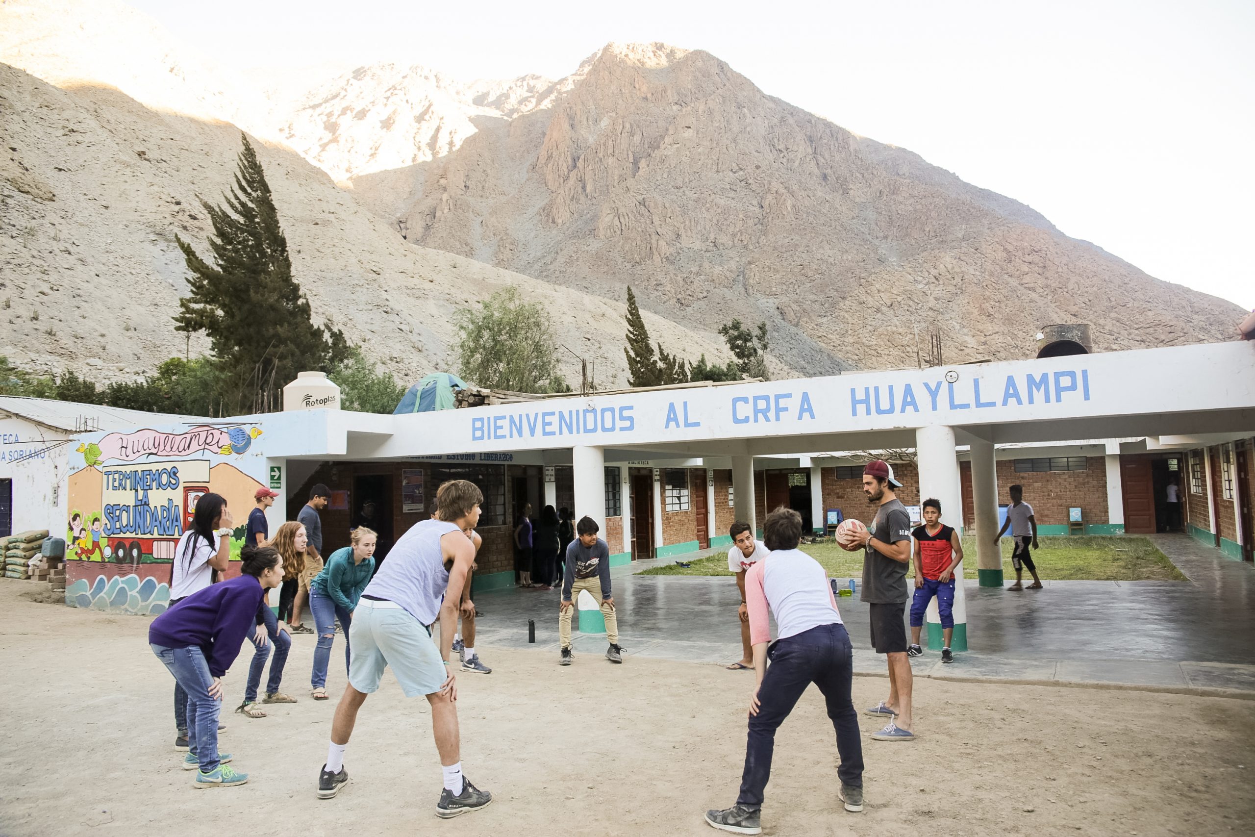 Students and adult playing ball together in front of a school in Peru.