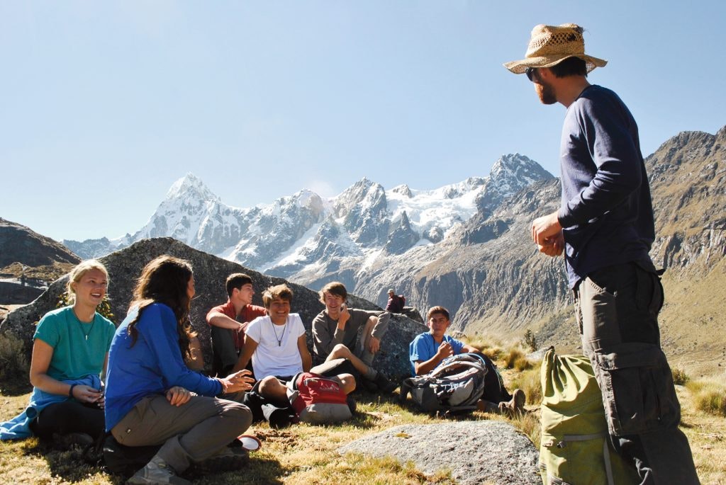 Group of hikers resting in front of snowy mountain peaks.