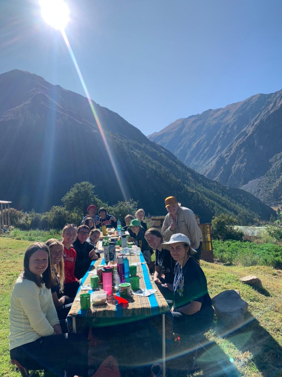 A school trip stops for a meal at a long outdoor table in the Andean valley