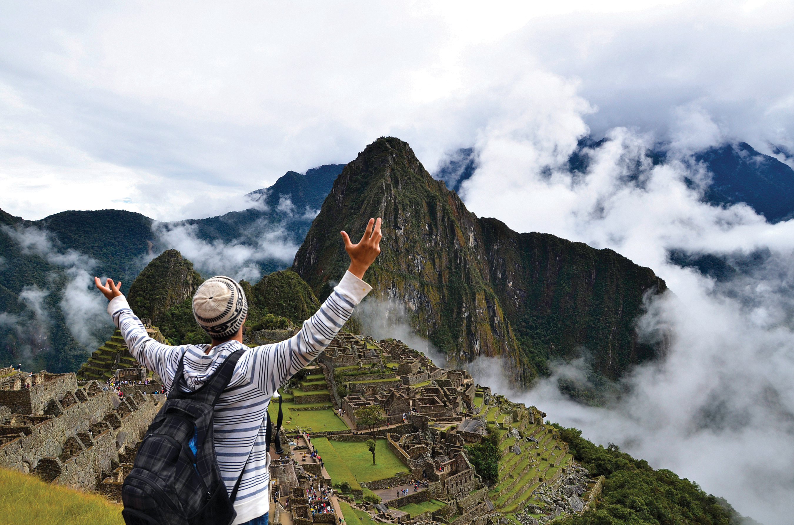 Person raising arms in awe while overlooking the ruins of Machu Picchu surrounded by clouds.