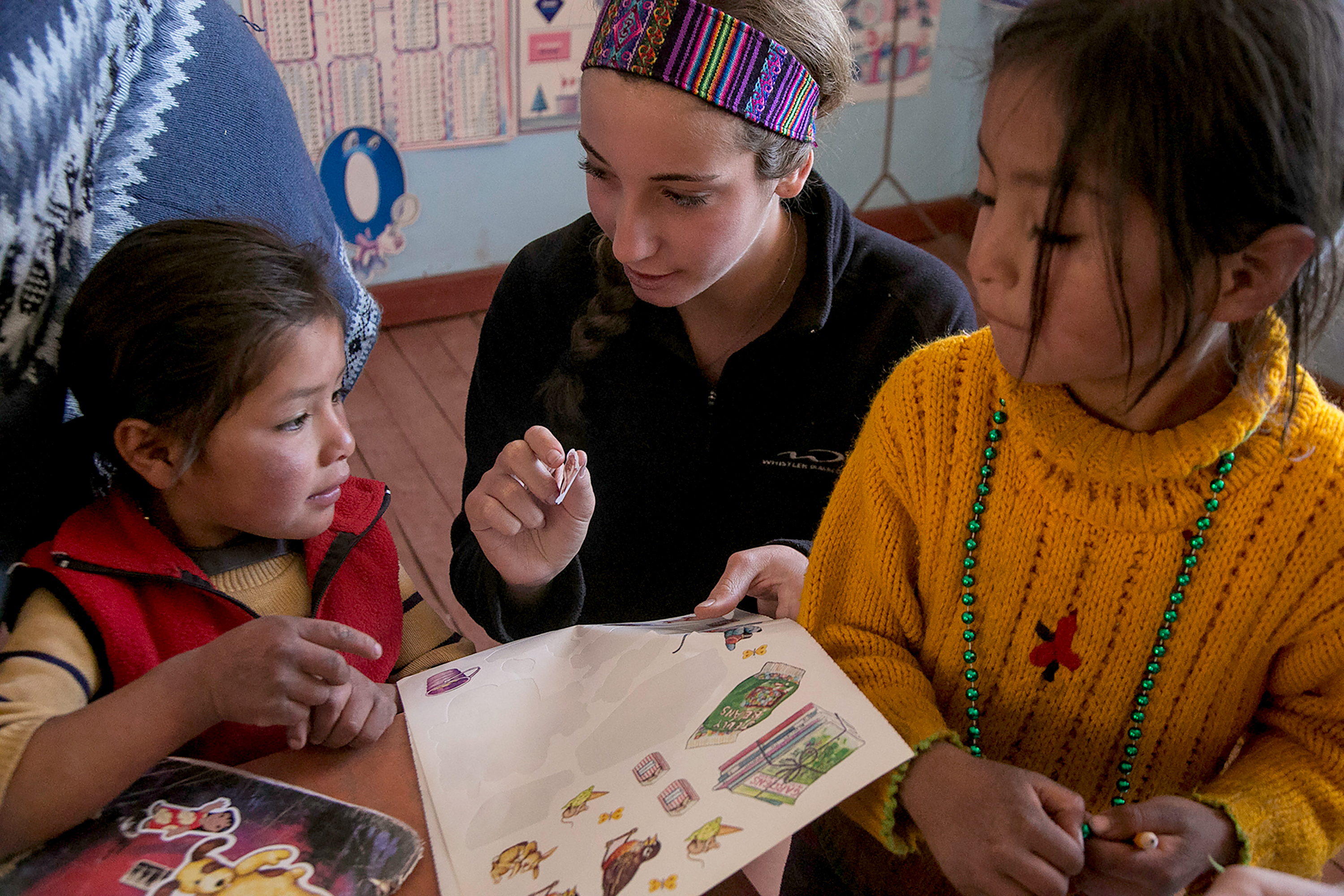 Teens on the trip show local children a coloring page at a table