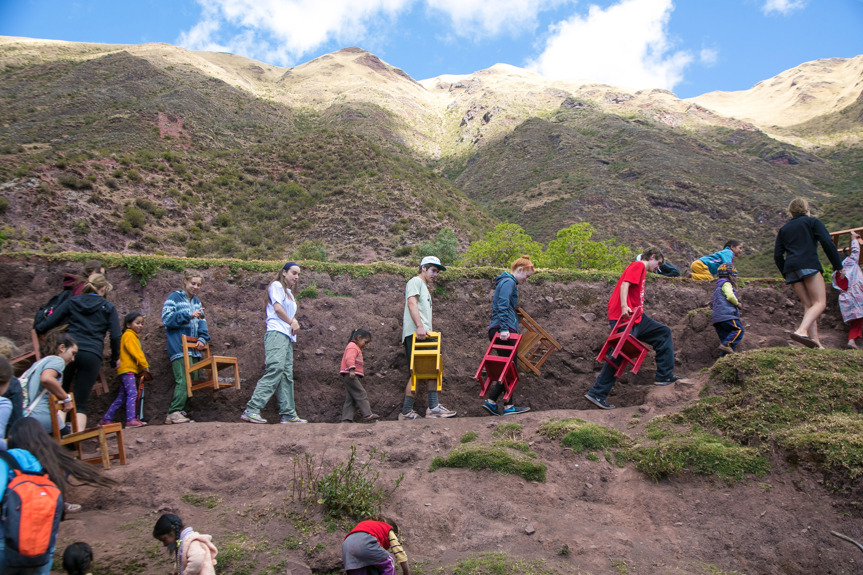 Students carry chairs along a mountain path in the Sacred Valley