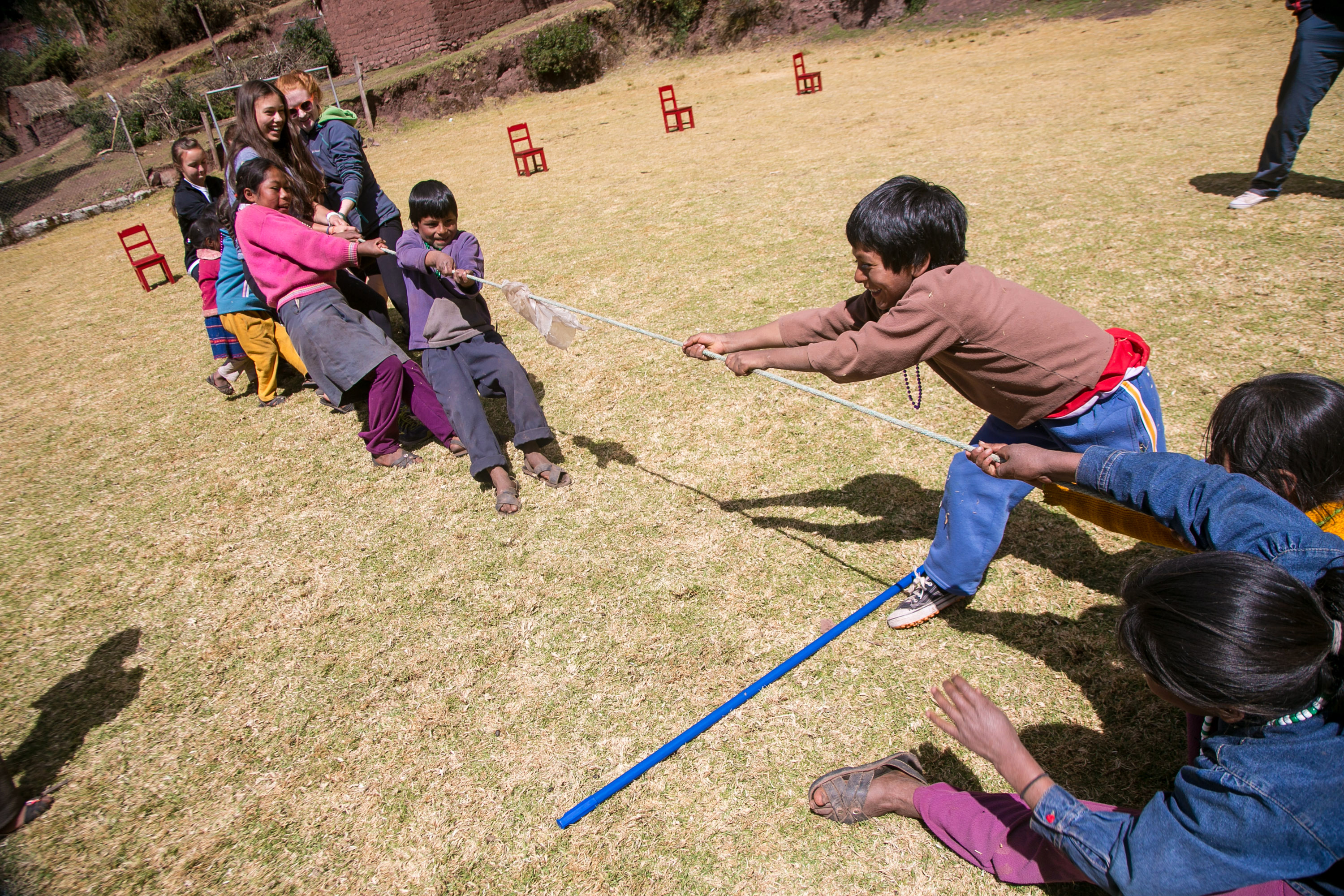 On this school trip, children play tug-of-war with a rope in a grassy field