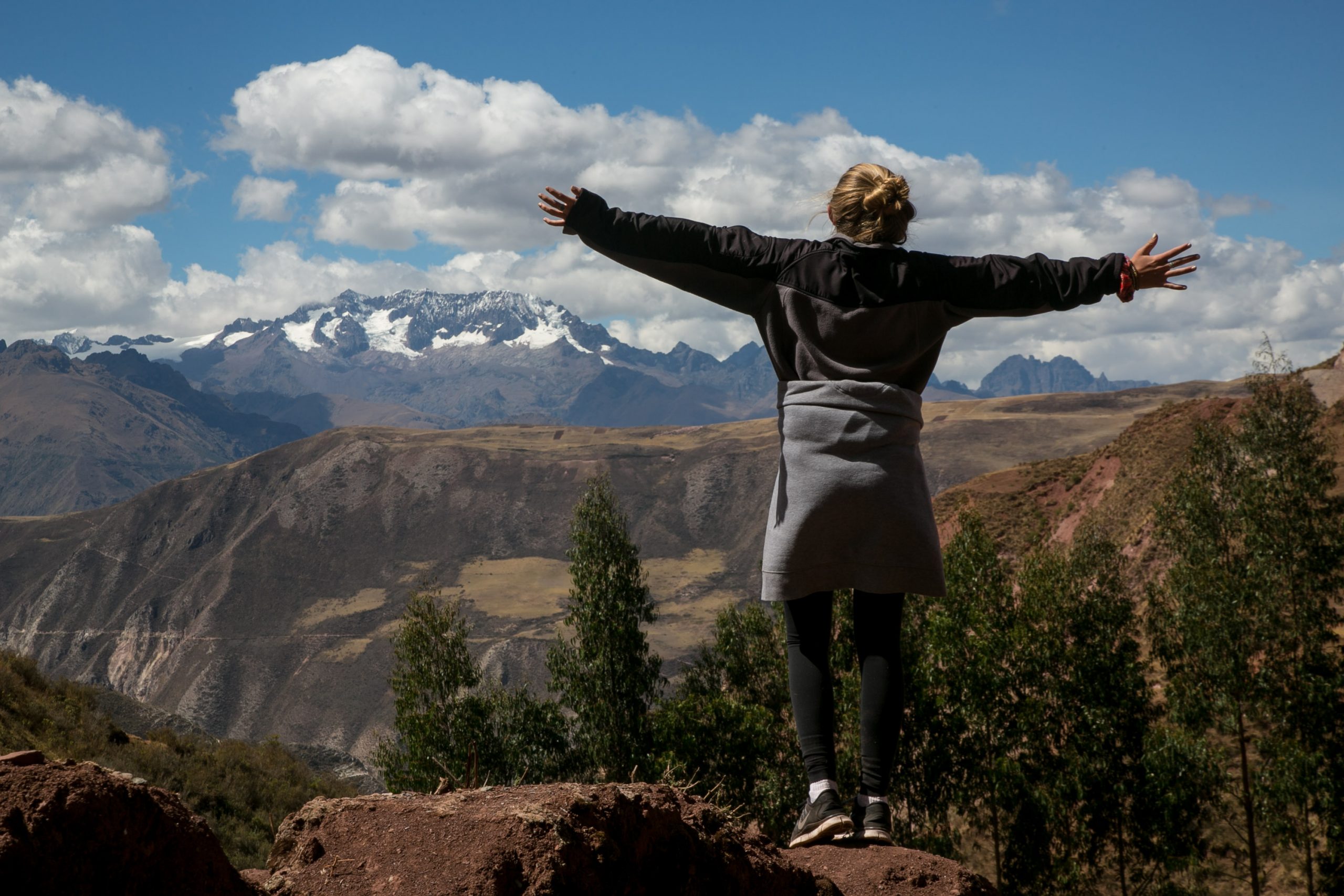 Person standing on a cliff with arms outstretched, admiring the mountain view. ￼