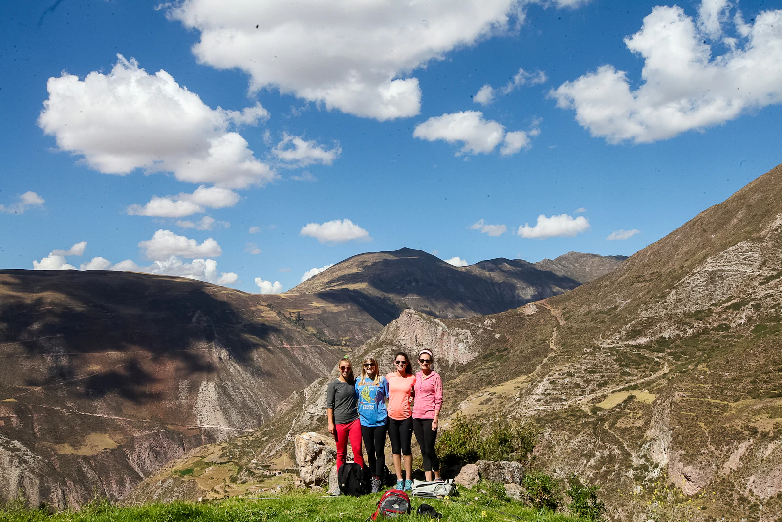 Four teen travelers stand together on a grassy slope above a deep, dry mountain valley in Peru